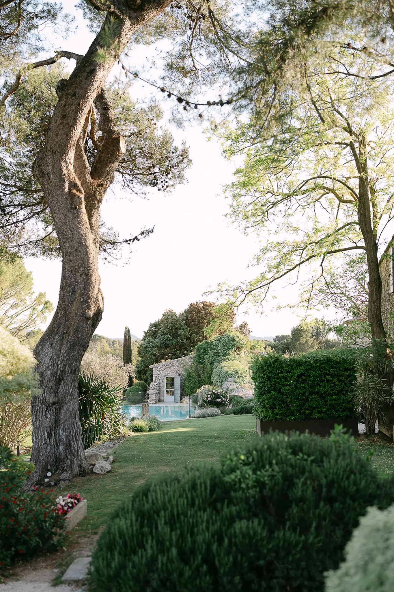 French estate grounds with pool, stone outbuilding, box hedging, bistro lights, and cypress tree