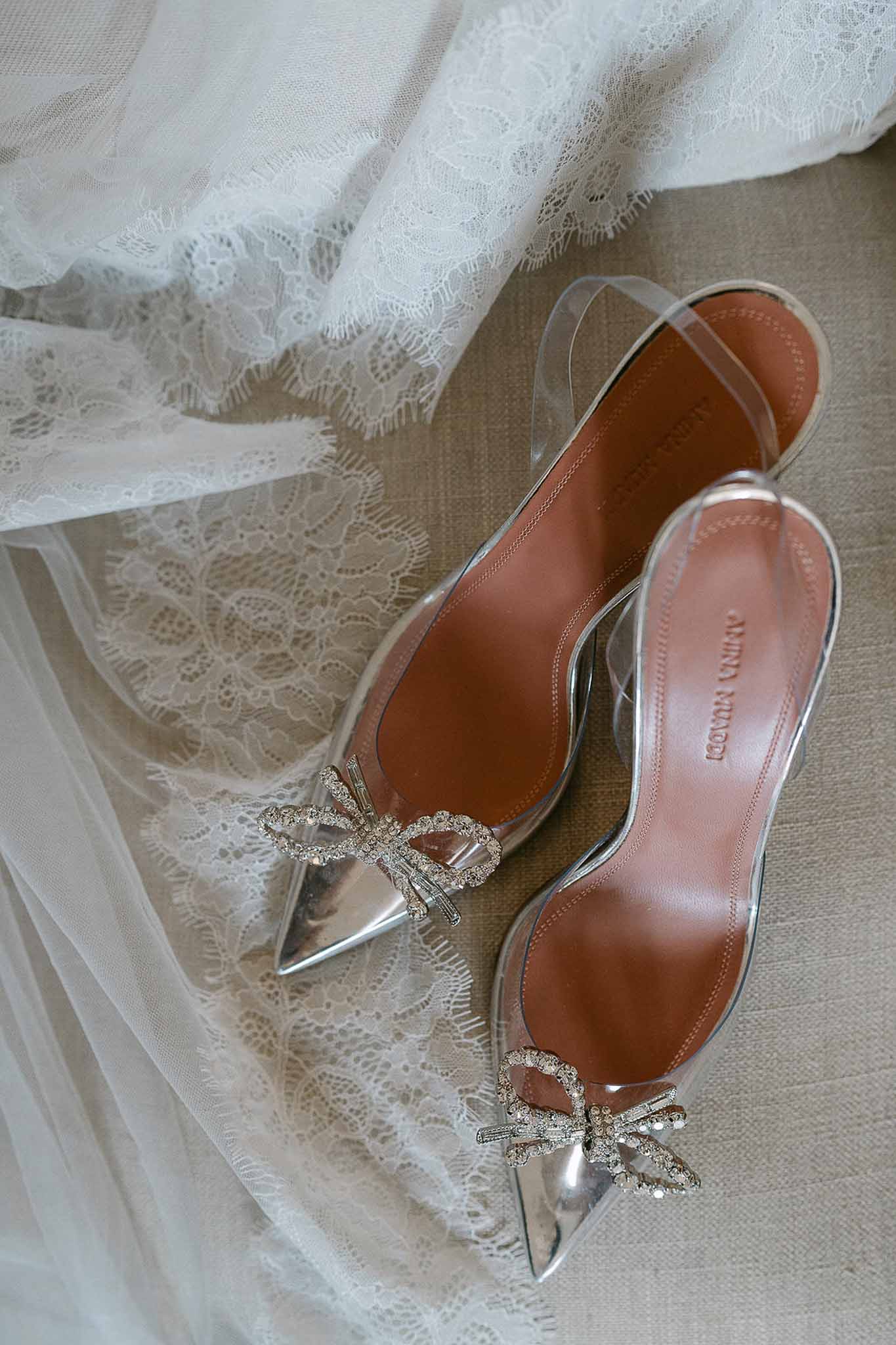 Amina Muaddi bridal heels with crystal bows and silver toe caps alongside white lace-trimmed veil