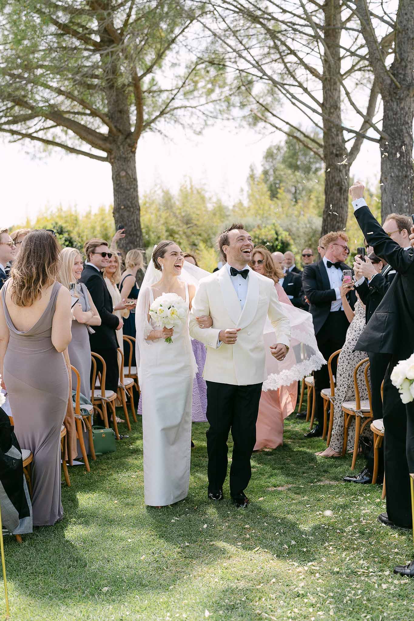 Couple recessioning with petal toss bride in ivory gown with cathedral veil groom in white dinner jacket
