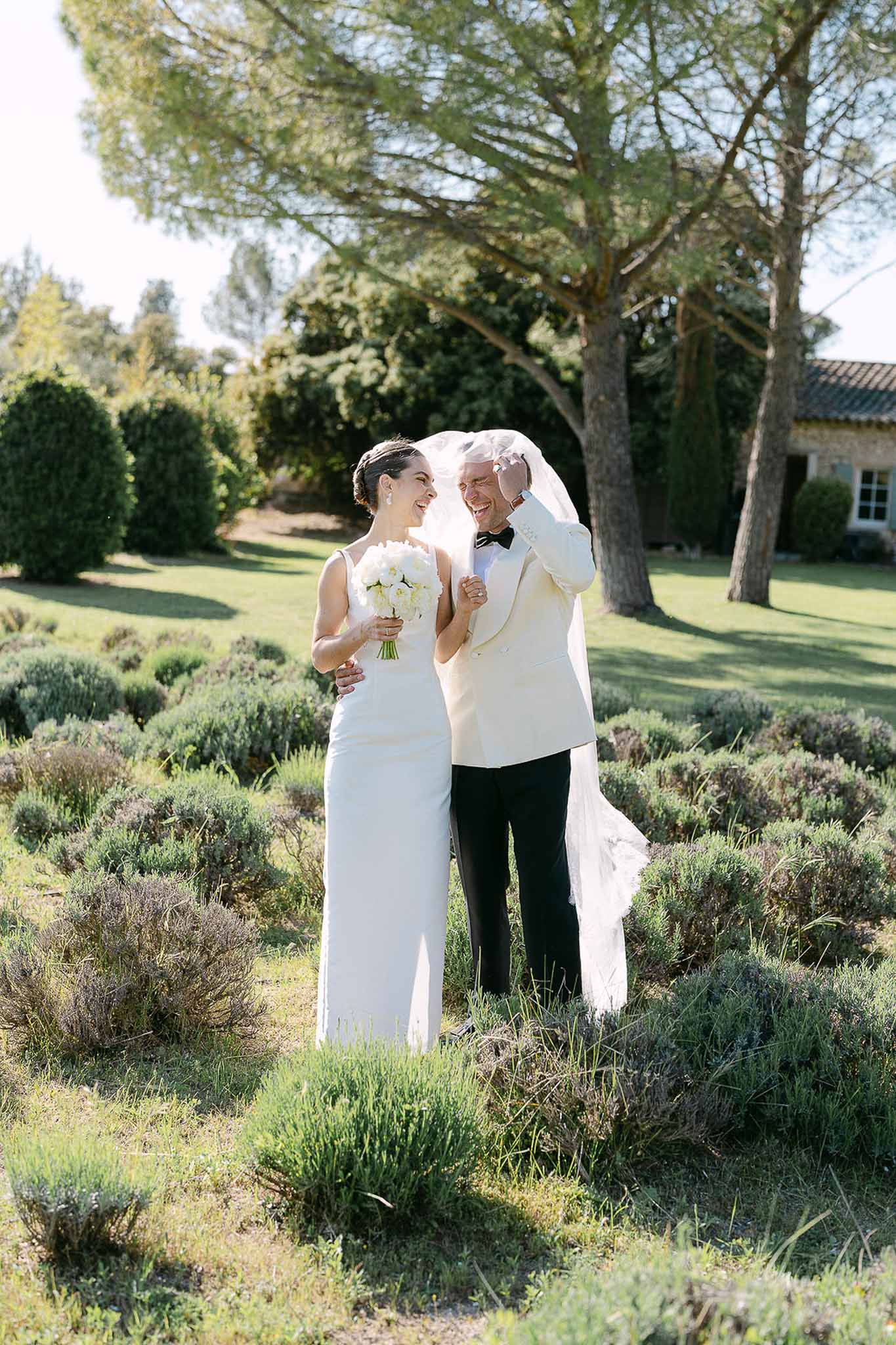 Bride and groom laughing among lavender bushes as groom lifts her veil at a Provencal property