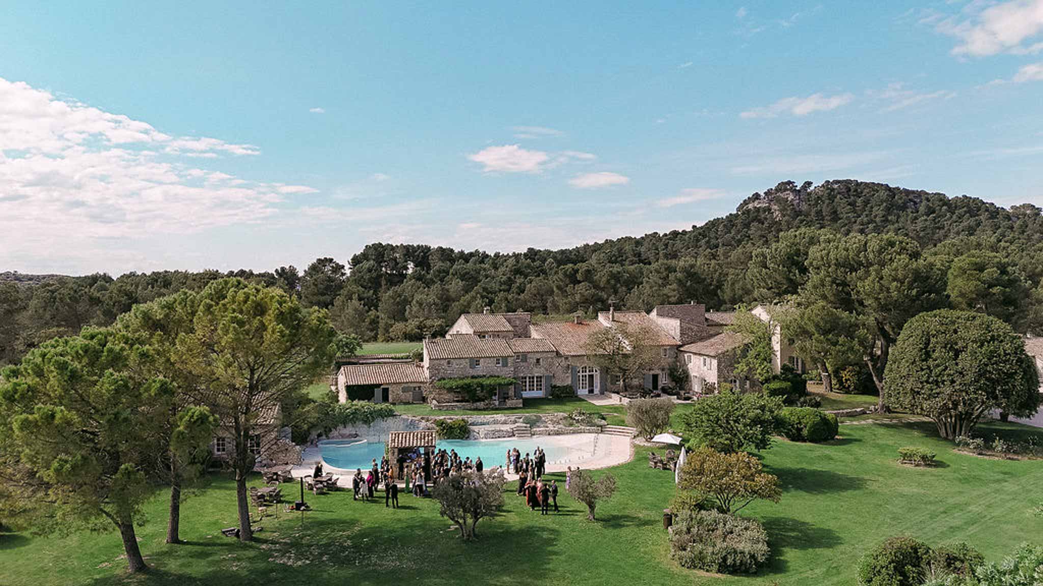 Aerial view of 40-50 guests at cocktail hour around a swimming pool at a stone mas property in the South of France