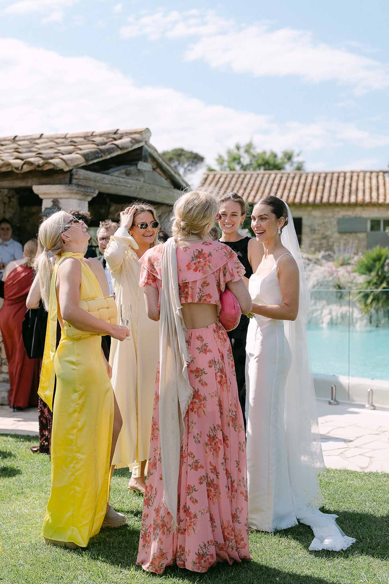 Bride in ivory slip gown chatting with guests by poolside at French country property during cocktail hour