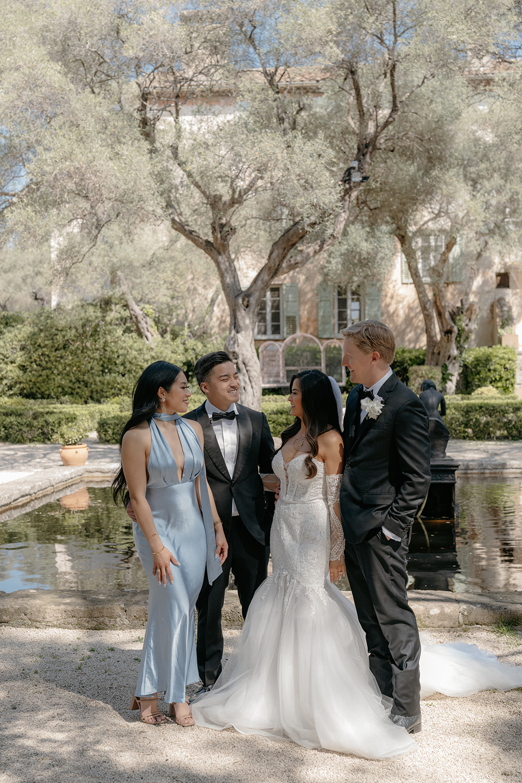 Bride groom and couple in blue satin dress and black tuxedo chatting by reflecting pool at Provencal villa