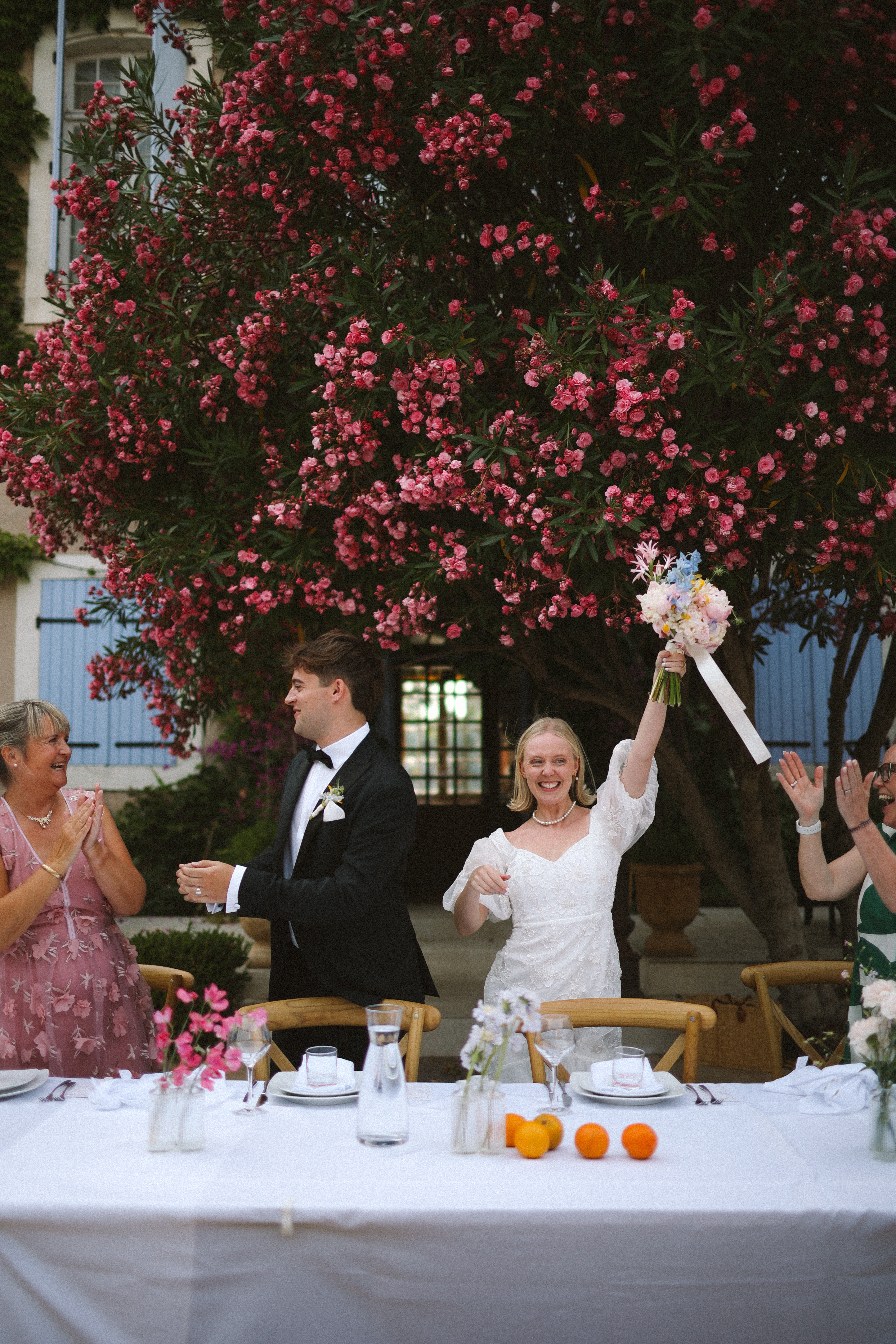 Bride cheering with bouquet at courtyard reception at Chateau du Puits es Pratx, Ginestas