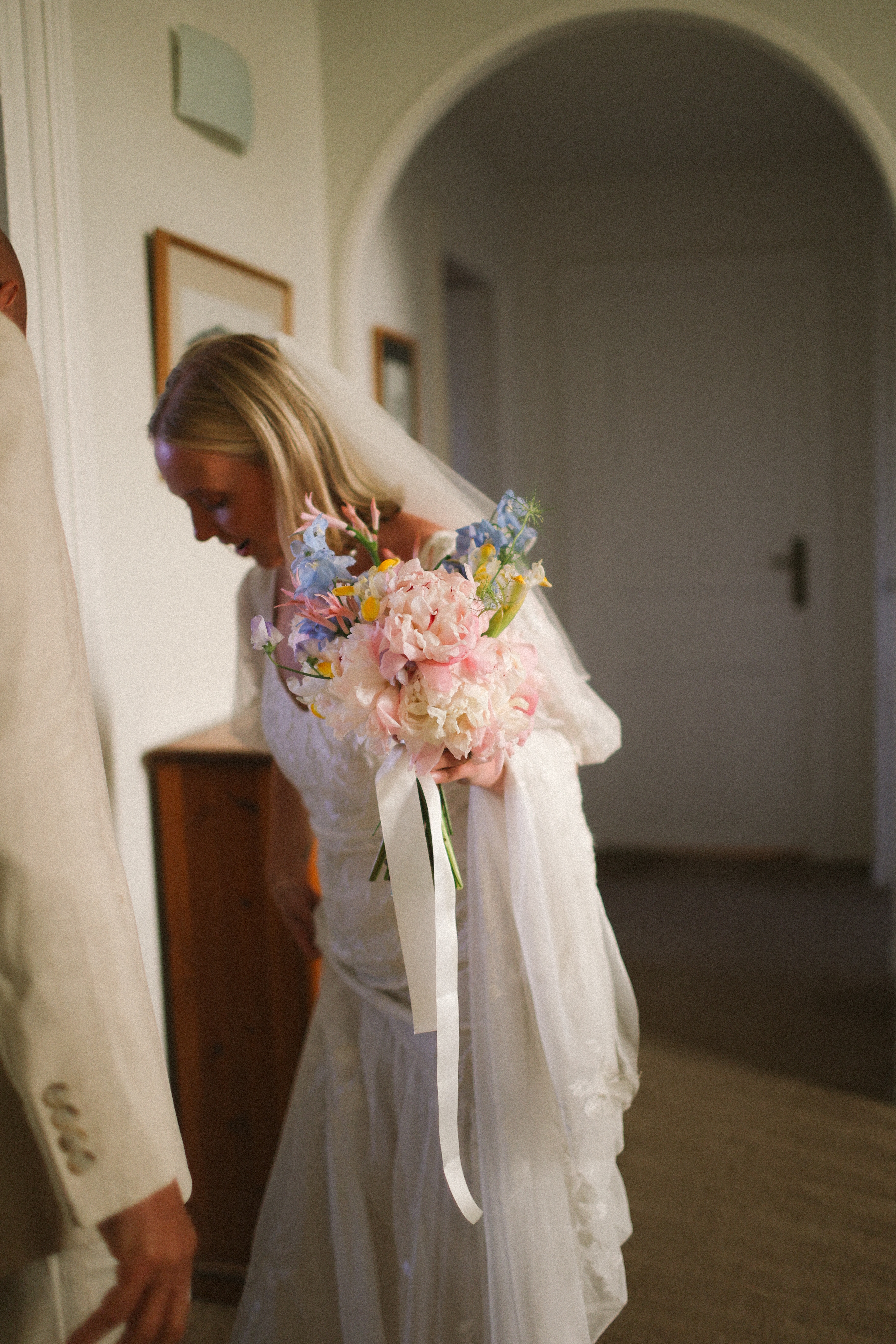 Bride admiring pastel bouquet in hallway at Chateau du Puits es Pratx, Ginestas