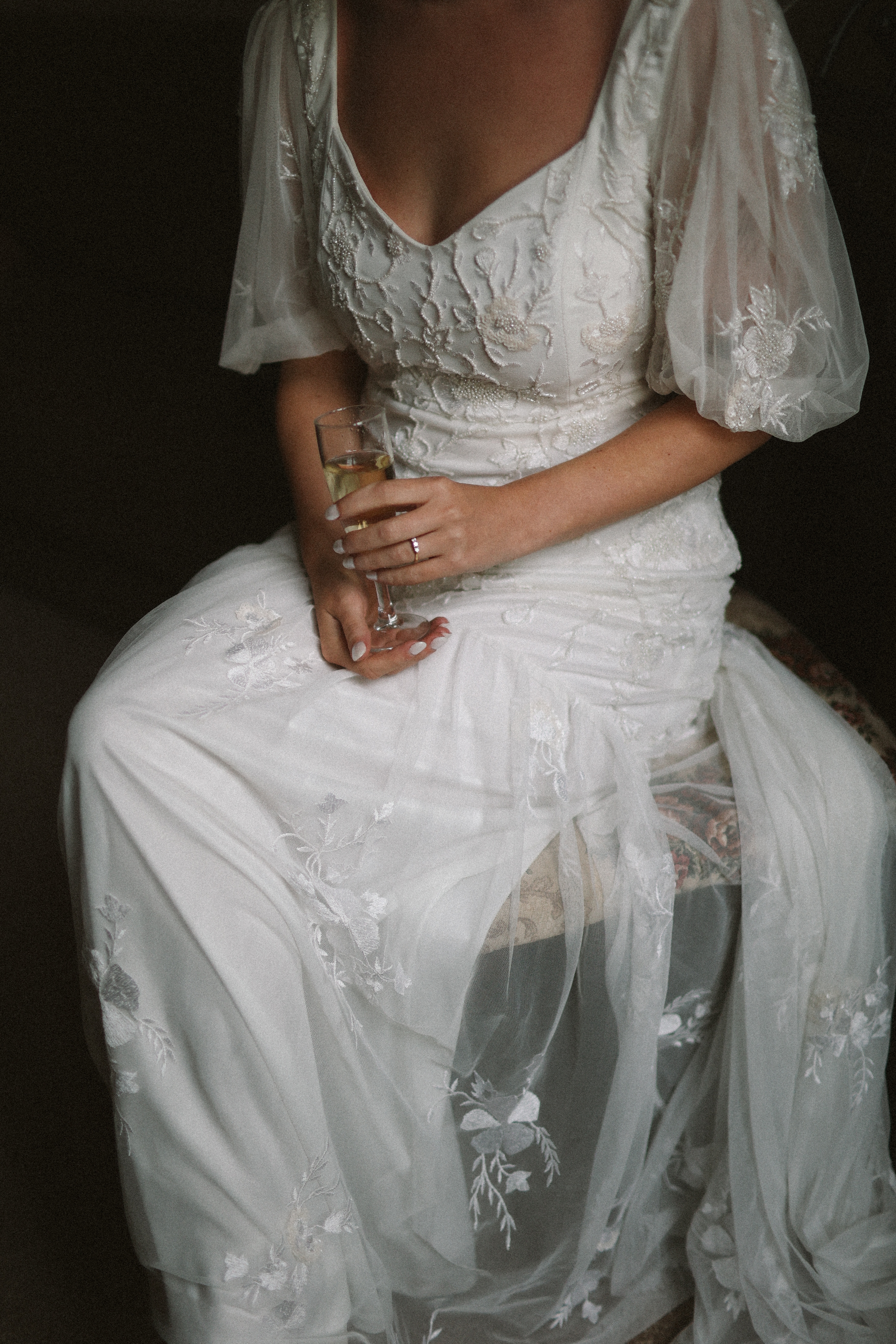 Bride seated in lace gown holding champagne coupe at Chateau du Puits es Pratx, Ginestas