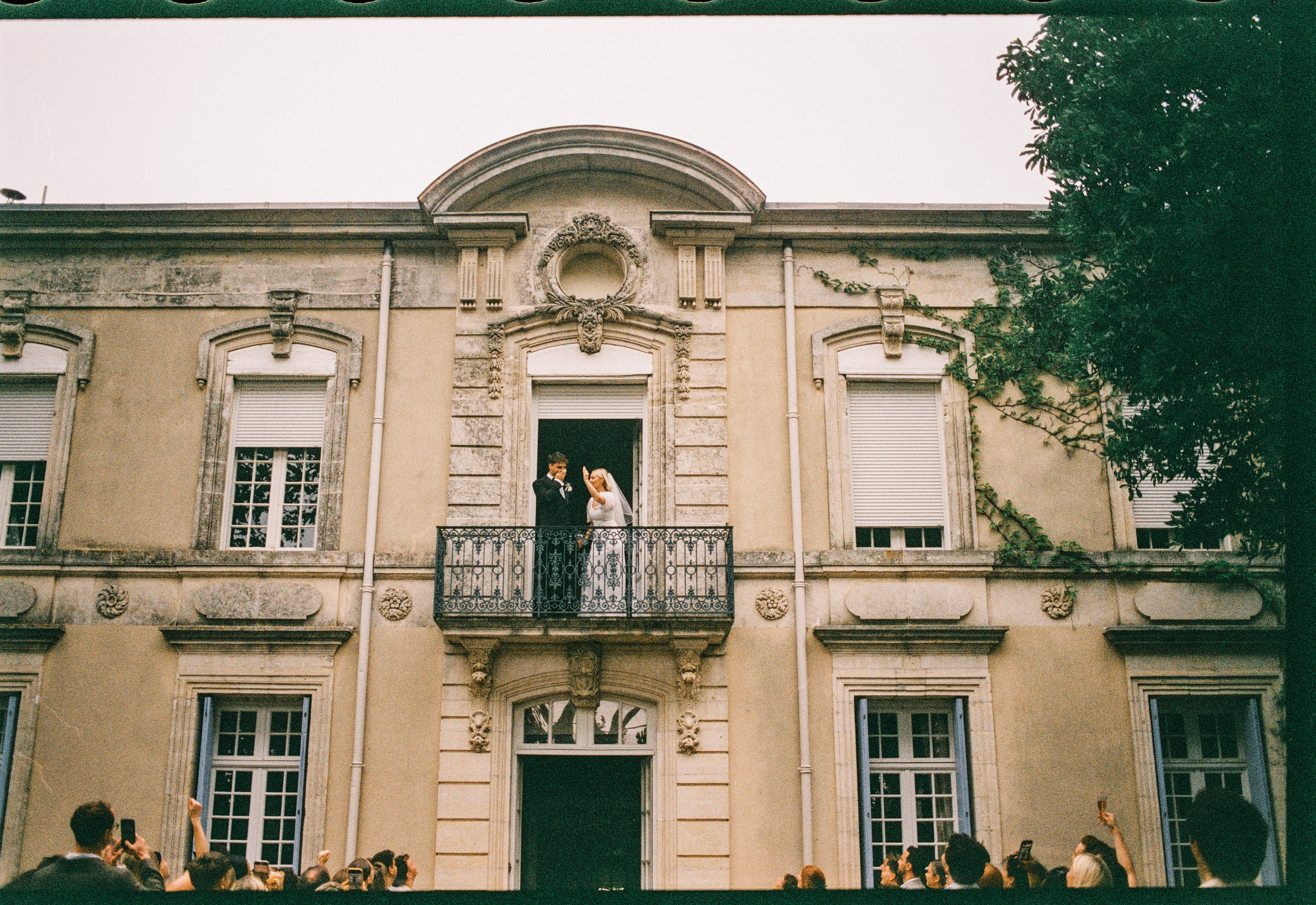 Bride and groom on chateau balcony with guests below at Chateau du Puits es Pratx, Ginestas
