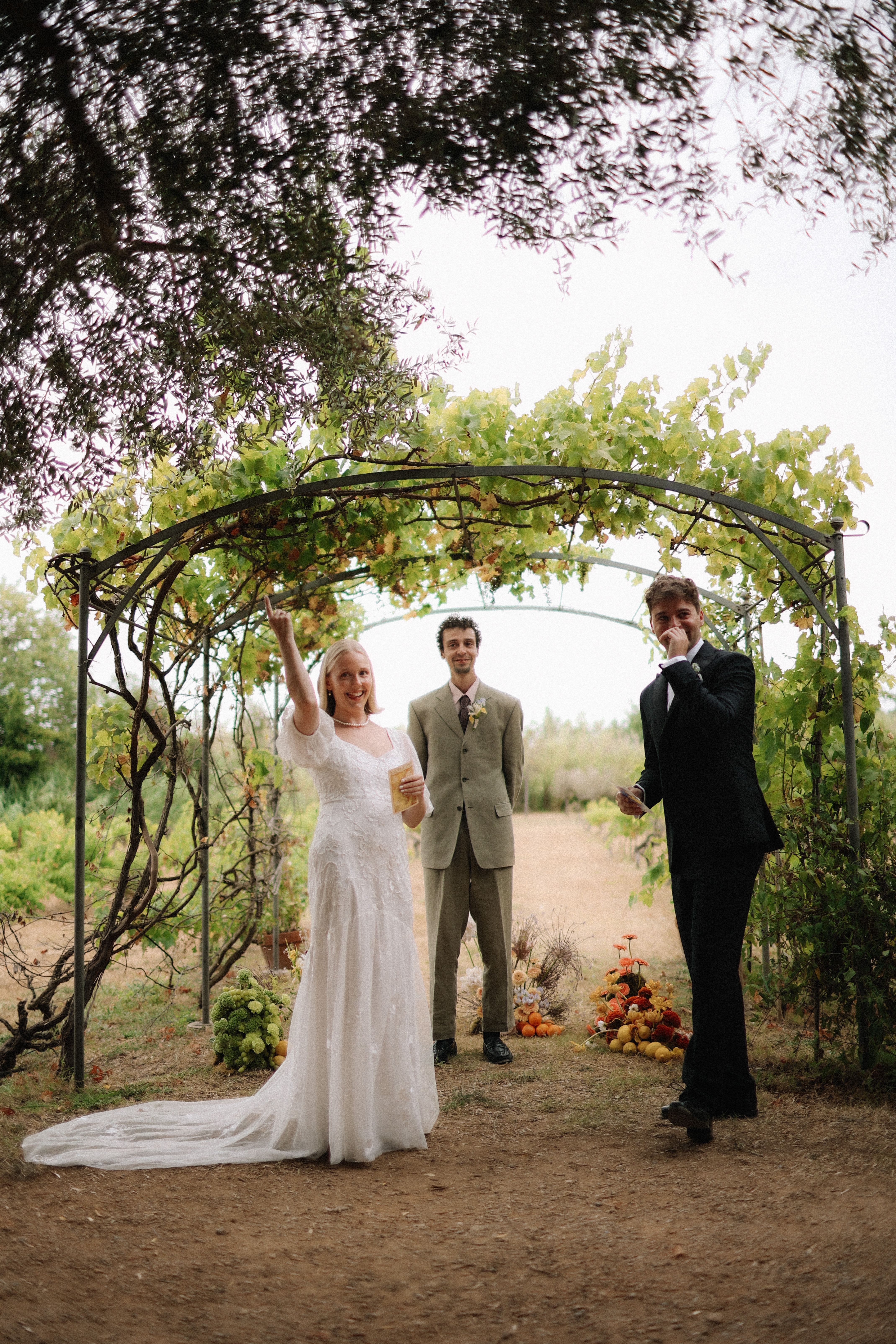 Bride laughs during ceremony under vineyard arch at Chateau du Puits es Pratx, Ginestas