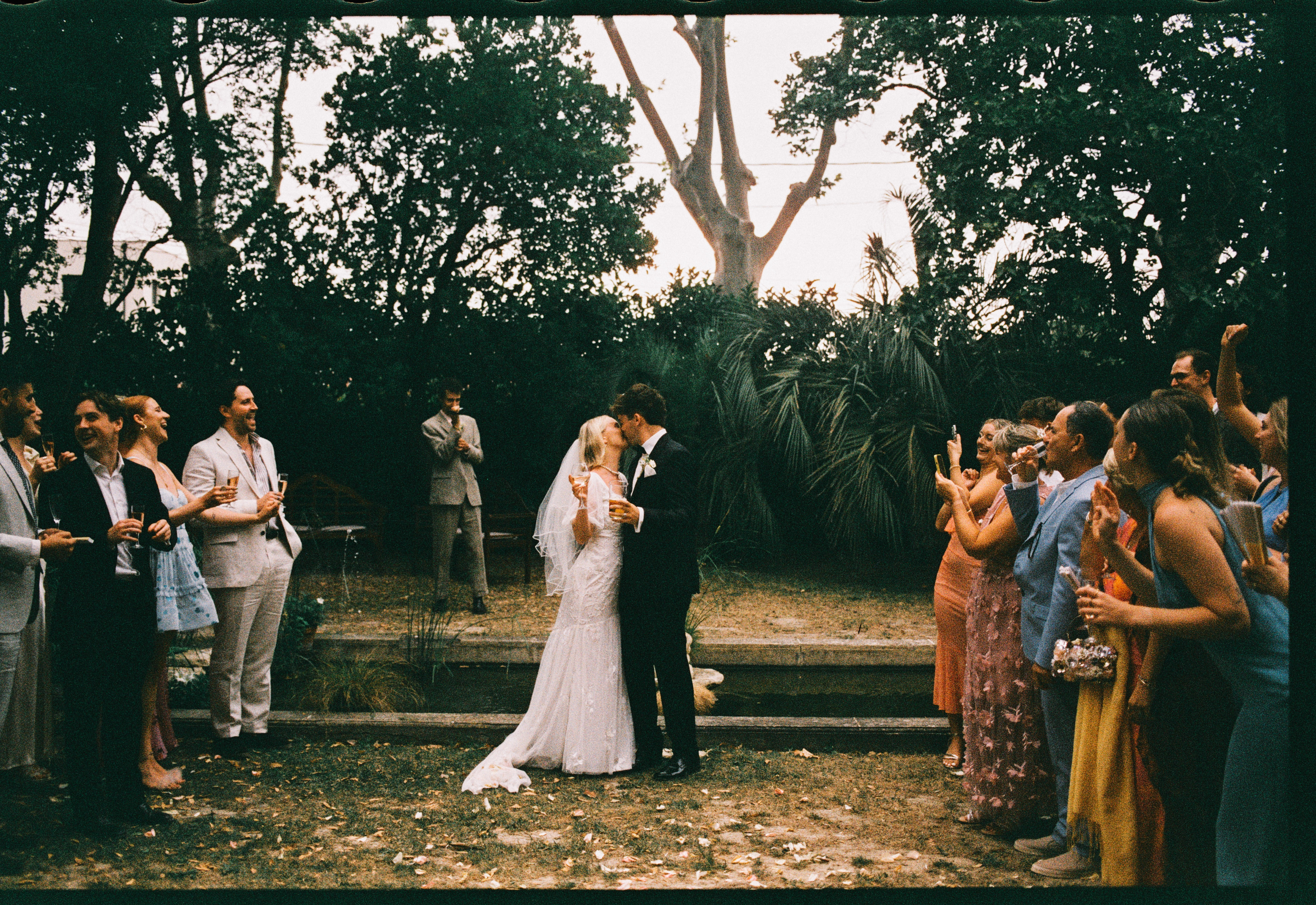 Couple kiss among cheering guests in garden at Chateau du Puits es Pratx, Ginestas