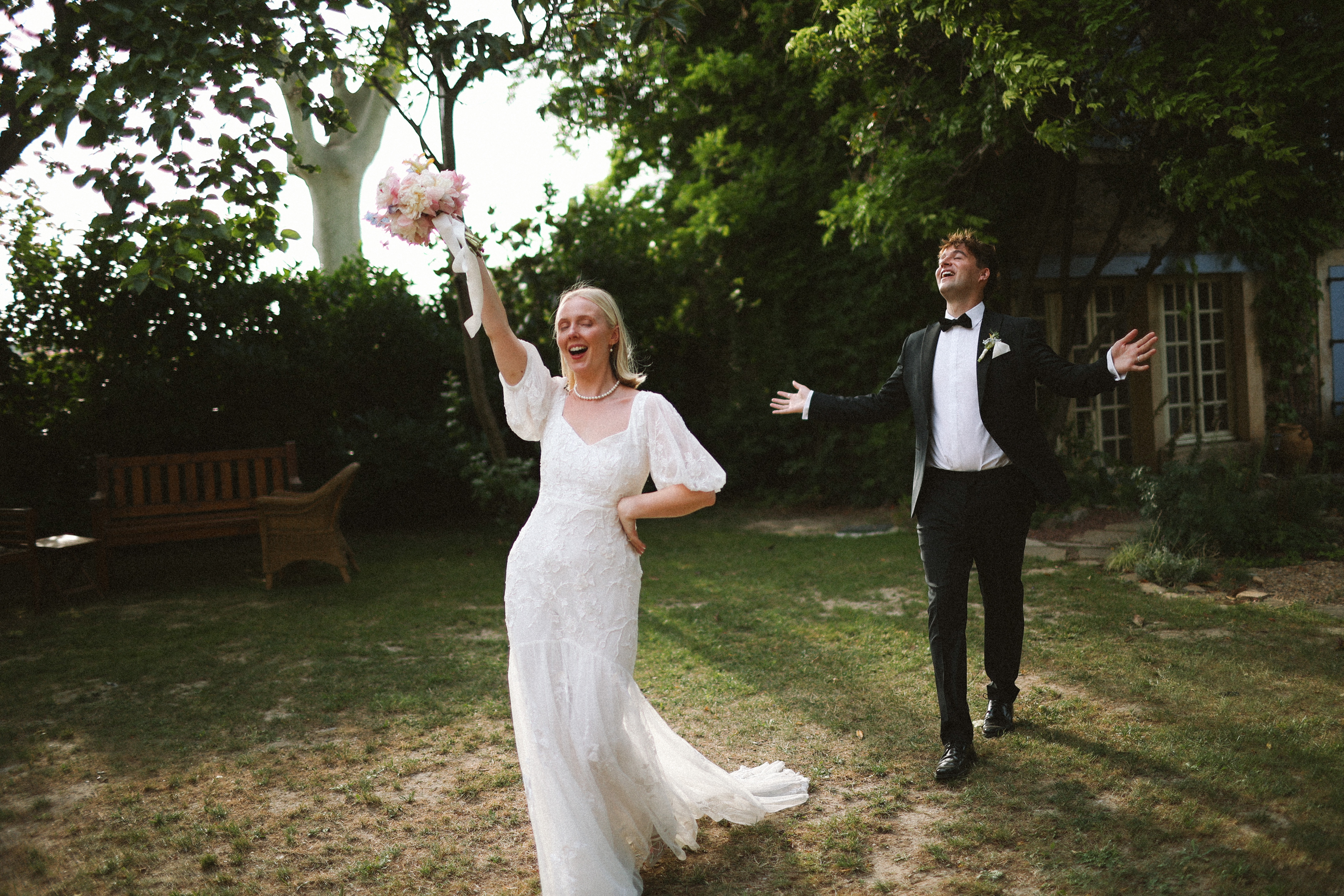 Bride cheering bouquet overhead beside groom at Chateau du Puits es Pratx, Ginestas