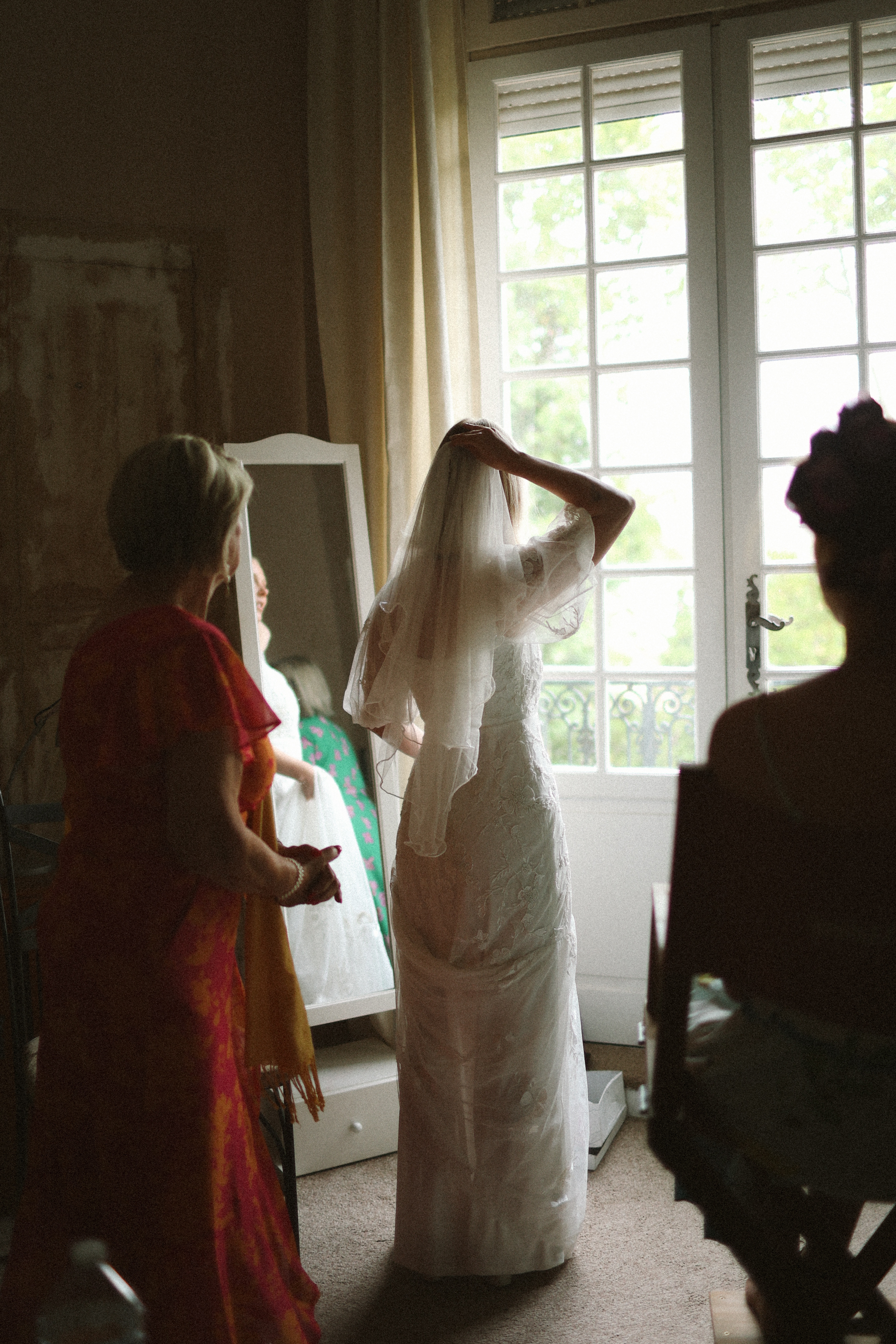 Bride adjusting veil at window with family at Chateau du Puits es Pratx, Ginestas