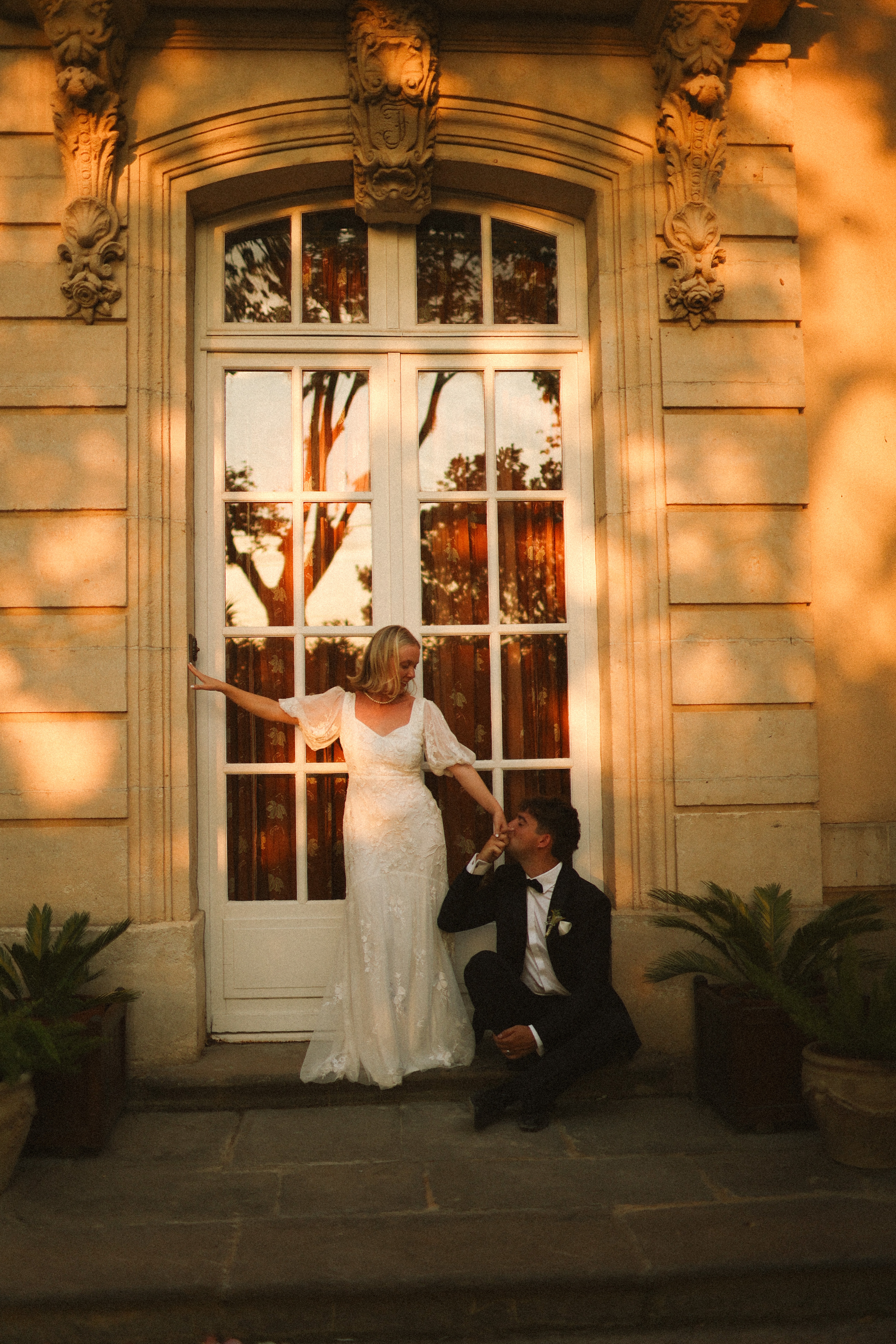 Groom kneeling kissing bride's hand at chateau doorway at Chateau du Puits es Pratx, Ginestas