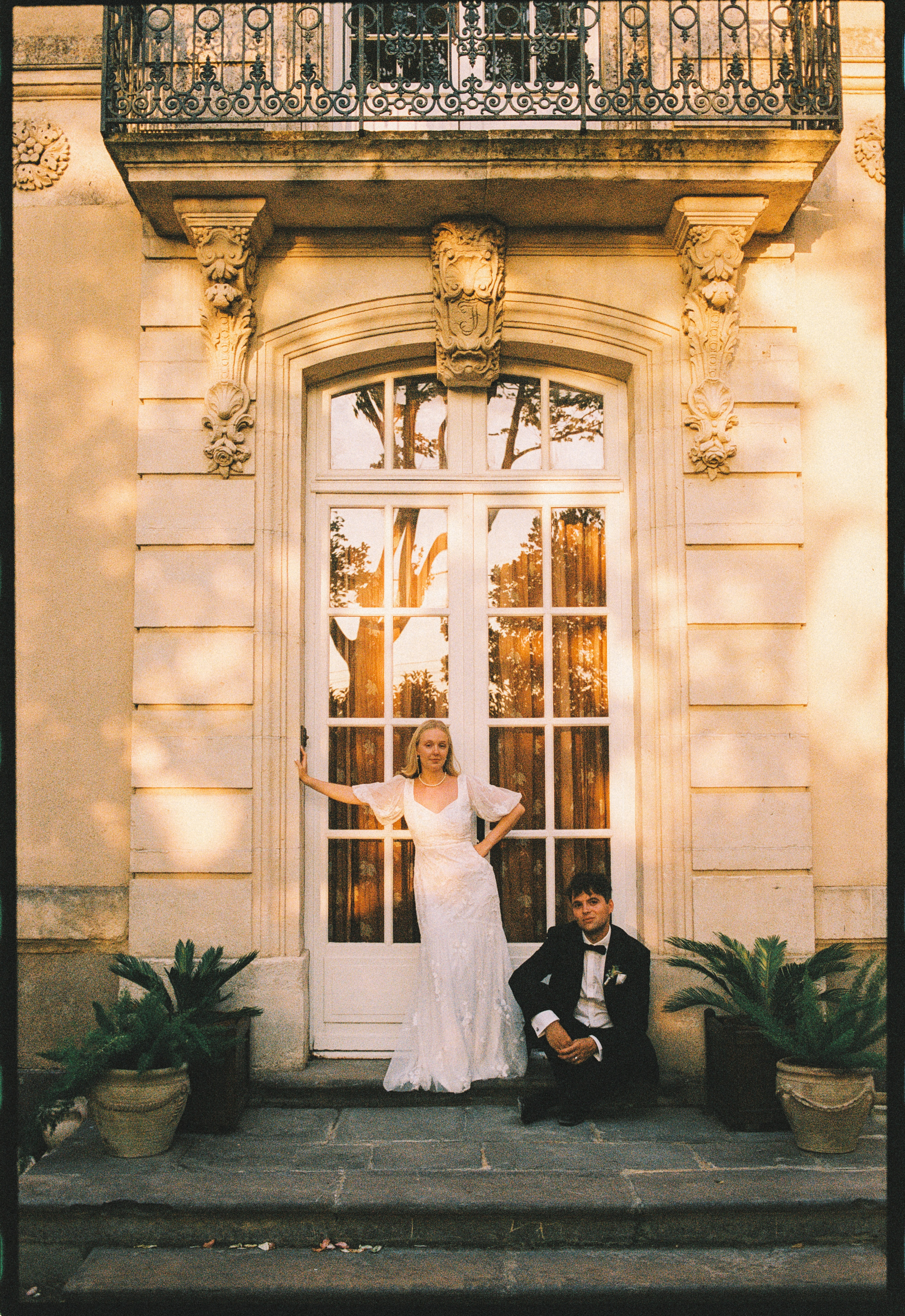 Bride standing groom seated at chateau doorway at Chateau du Puits es Pratx, Ginestas