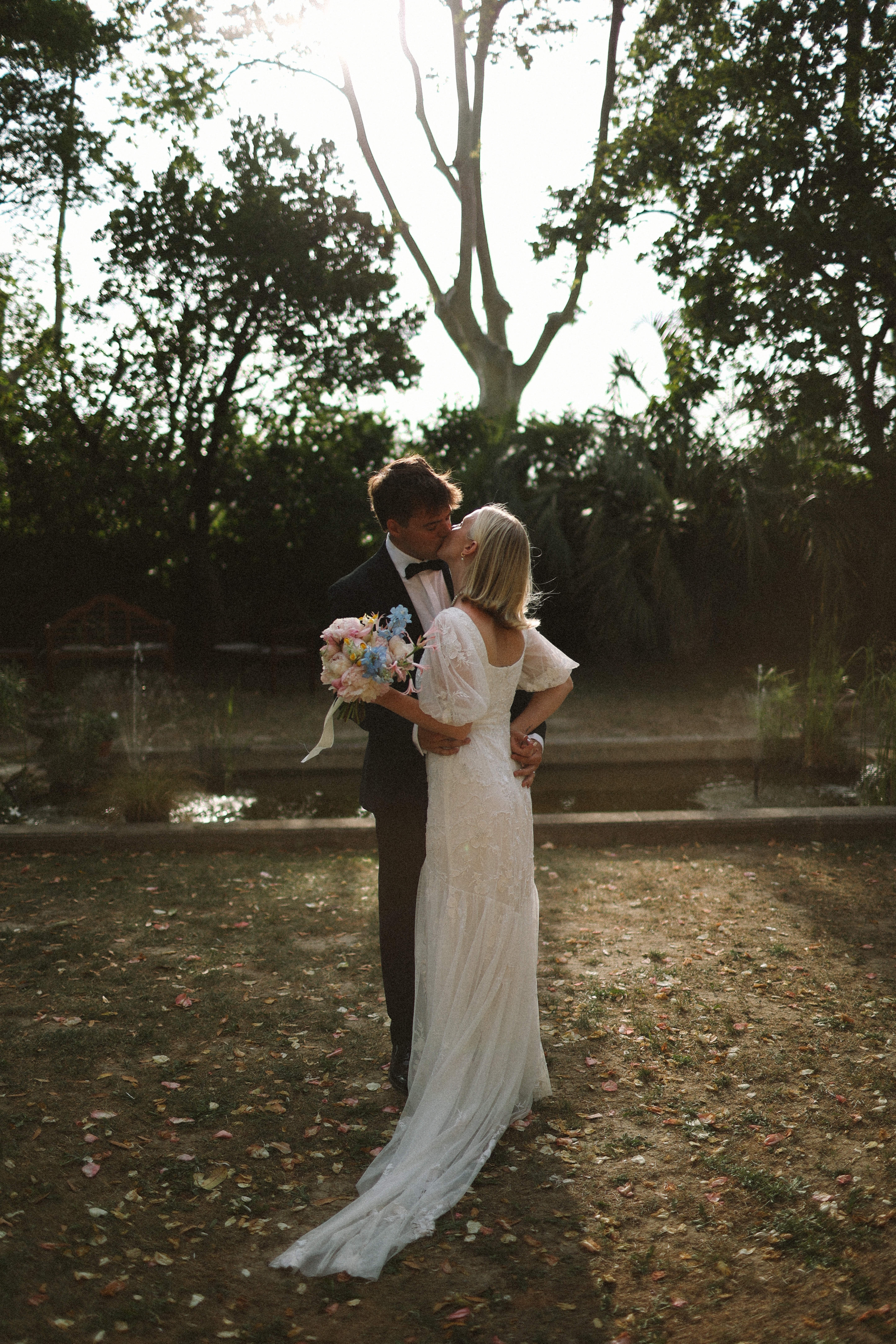 Couple kiss by pond beneath trees at Chateau du Puits es Pratx, Ginestas