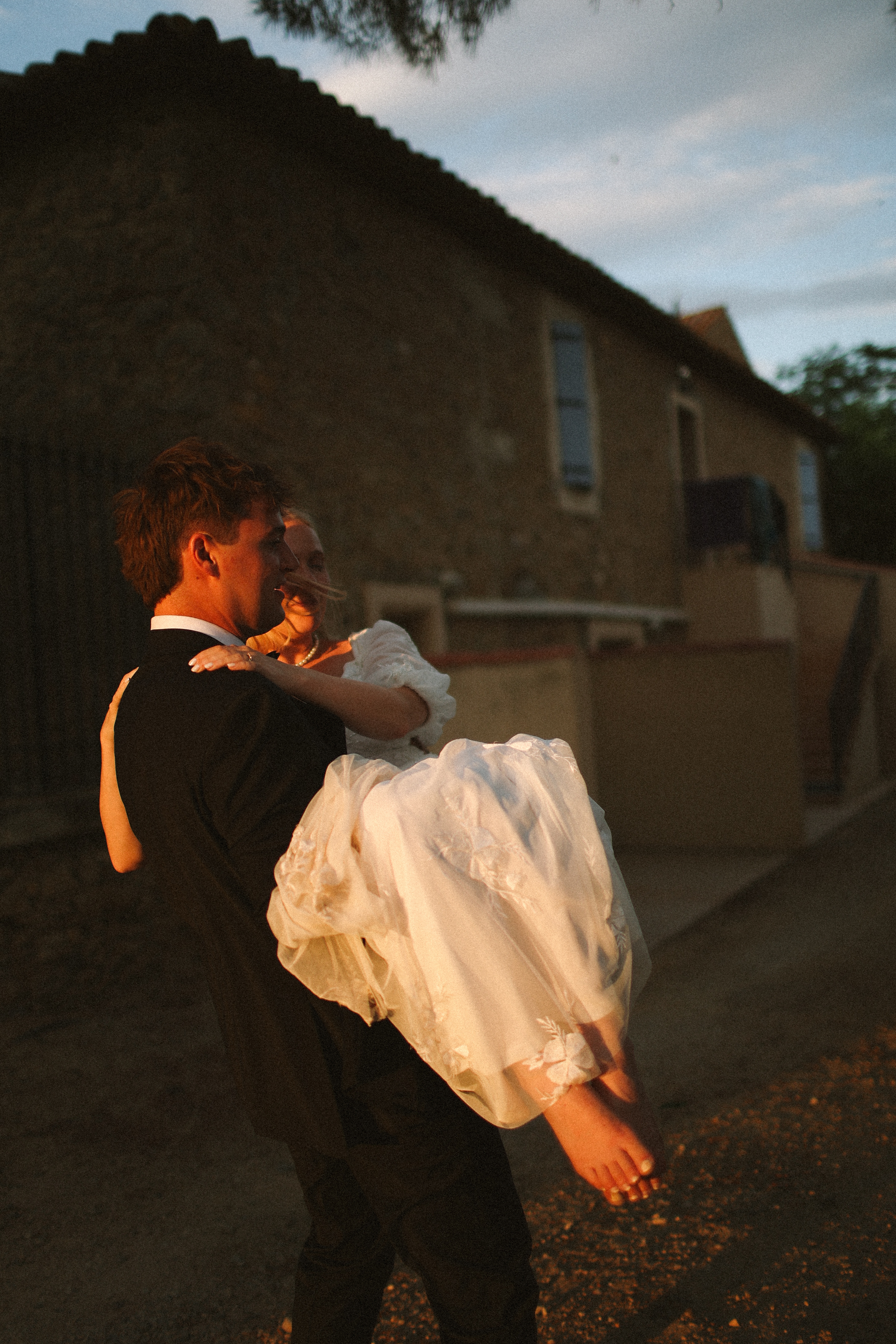 Groom carrying barefoot bride at dusk at Chateau du Puits es Pratx, Ginestas