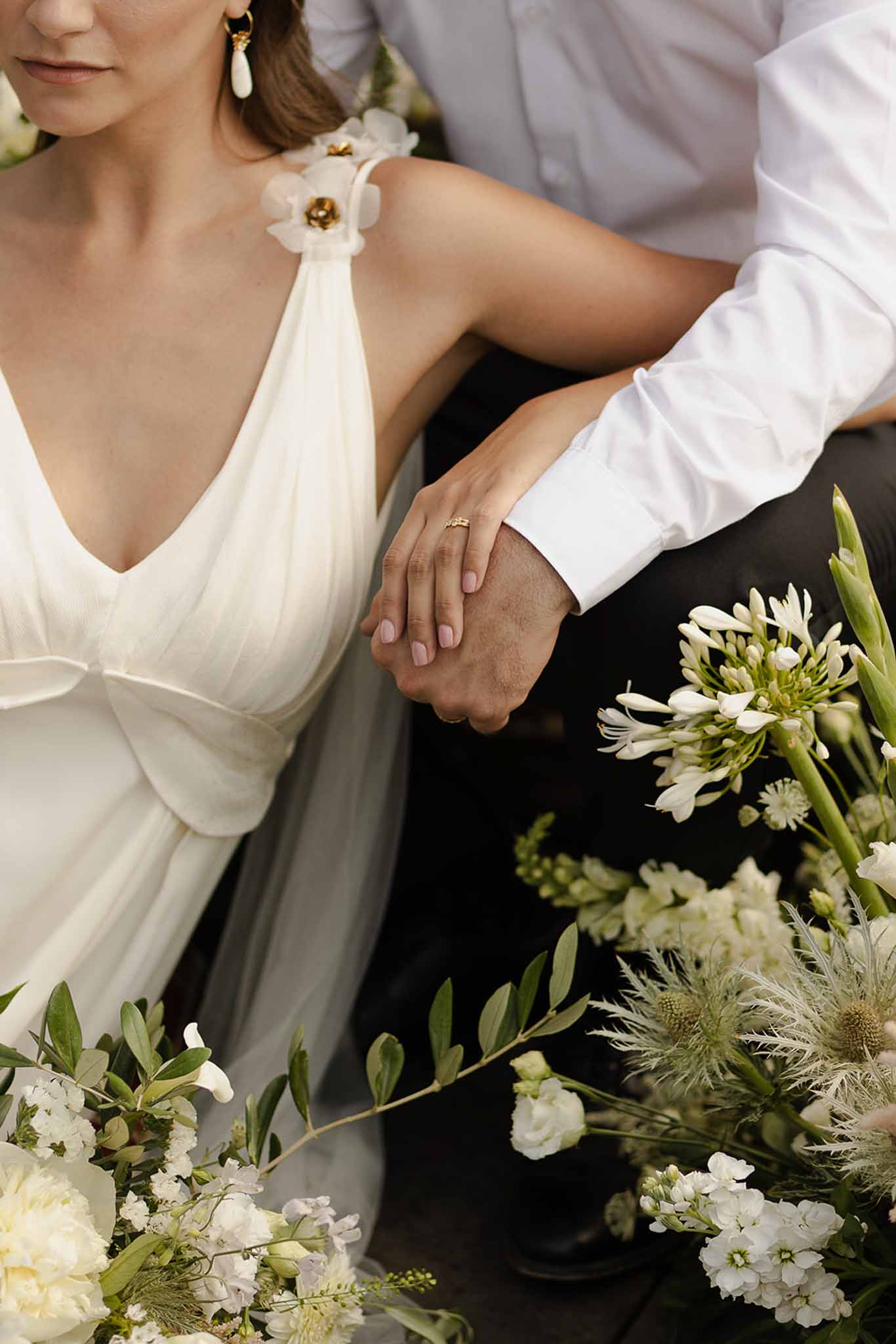 Couple's hands with wedding rings and white flowers at Plage d'Apremont-sur-Allier