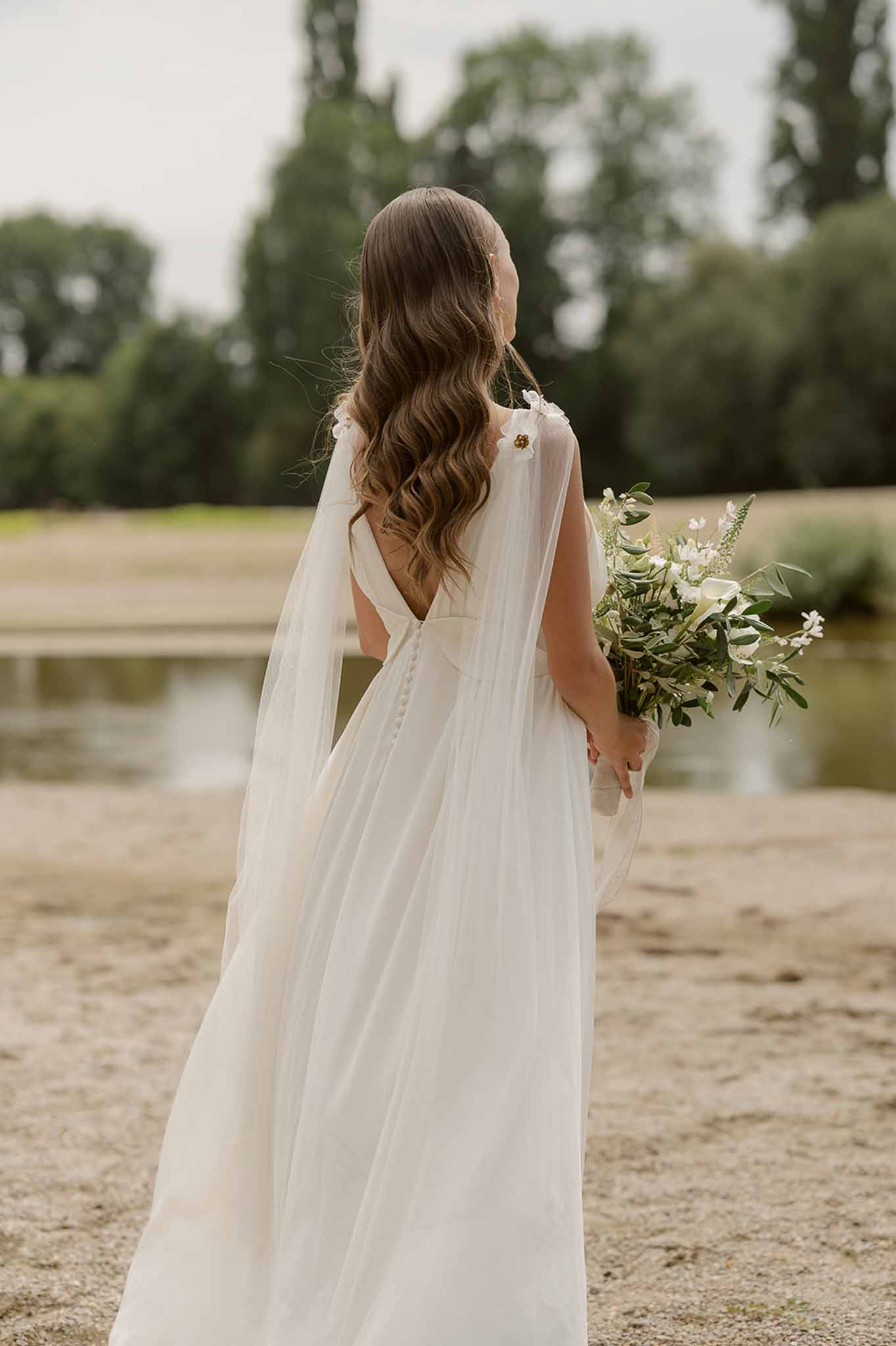 Bride with cape and bouquet from behind at Plage d'Apremont-sur-Allier