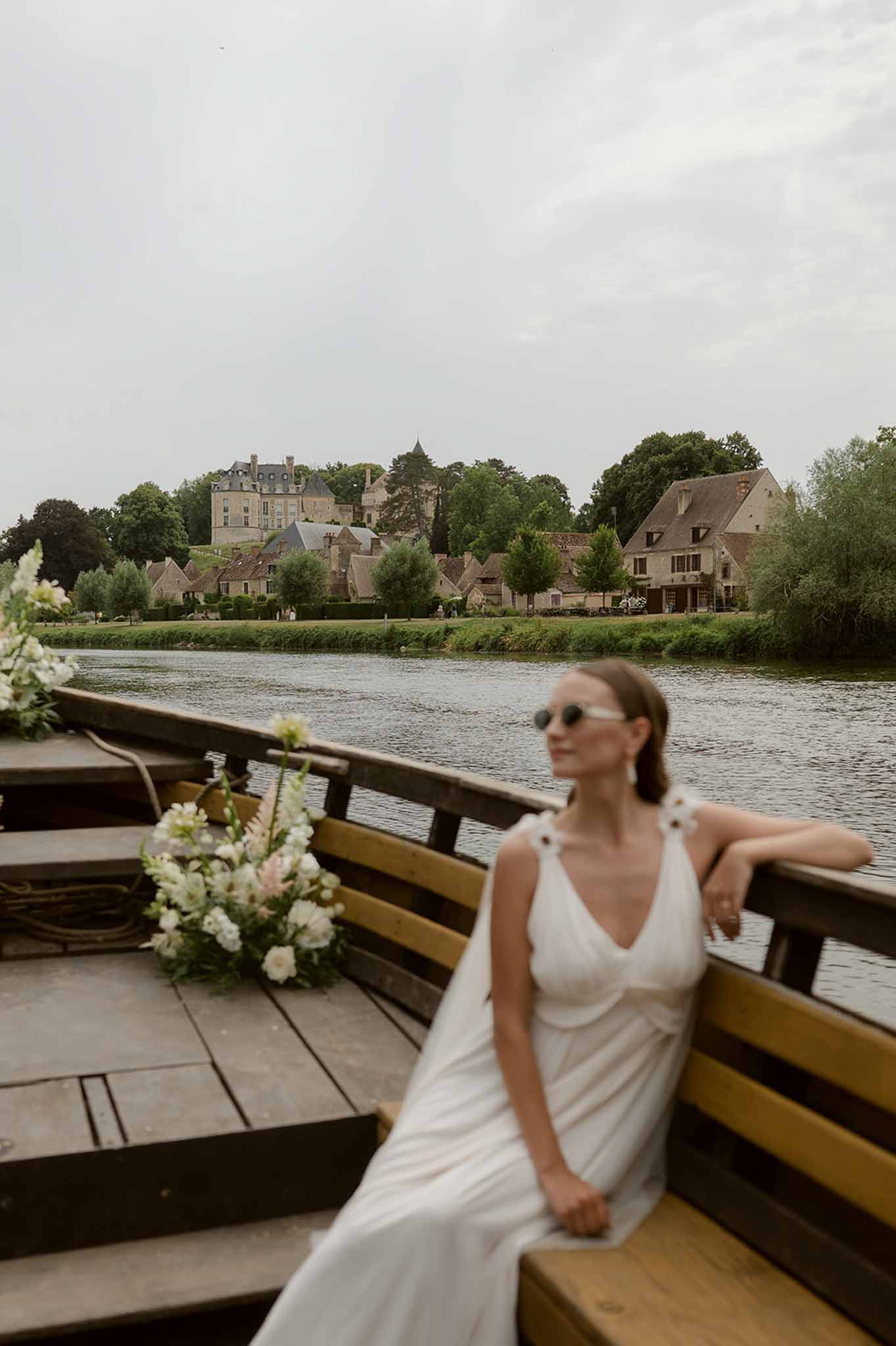 Bride in sunglasses on boat with Apremont chateau across river Burgundy