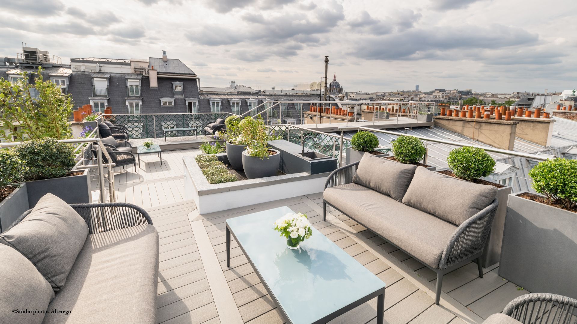 Parisian rooftop terrace with modern lounge furniture, topiaries, and Haussmann roofscape in background