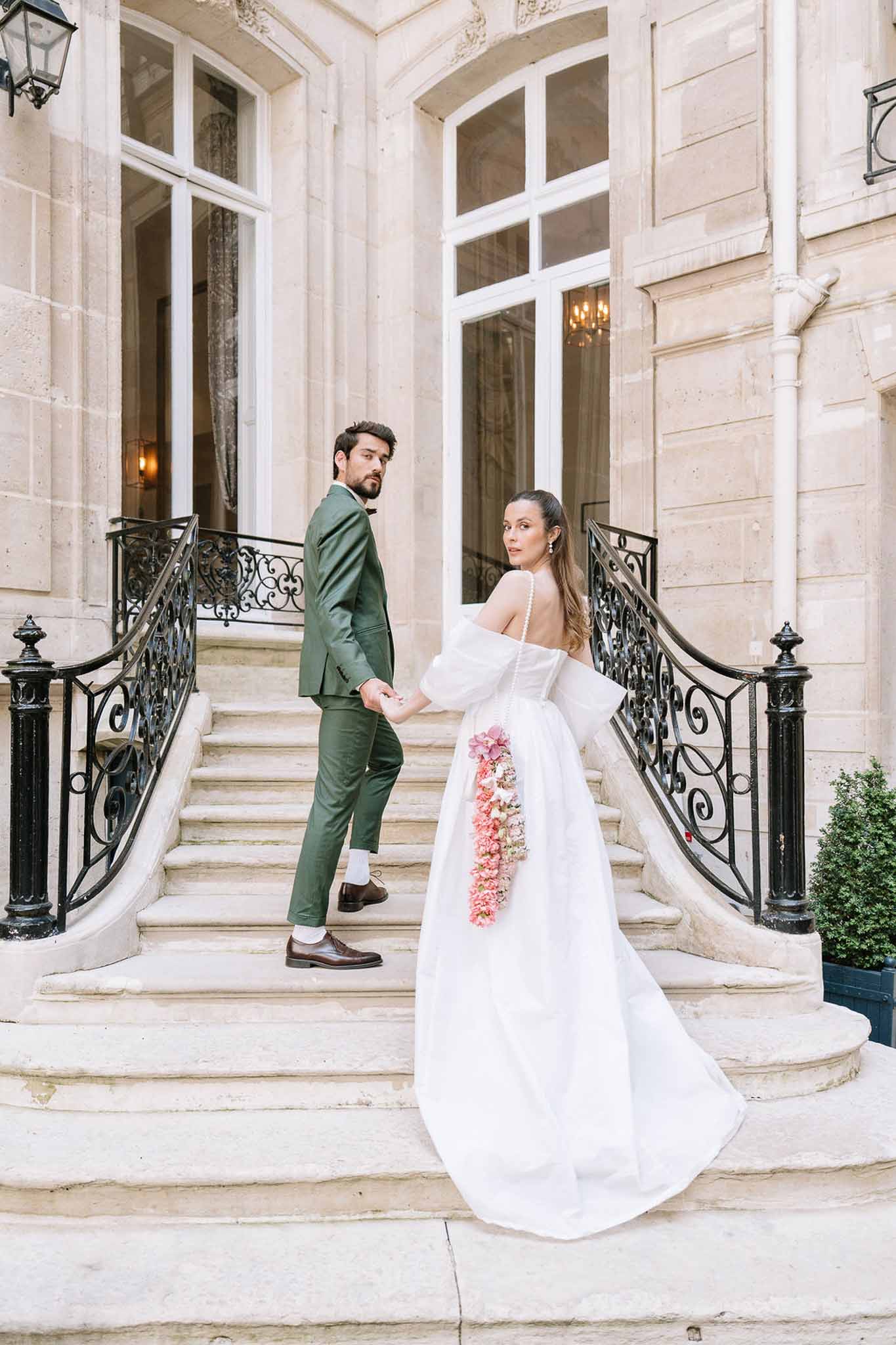 Groom in green suit and bride in off-shoulder ballgown with floral train posing on stone staircase