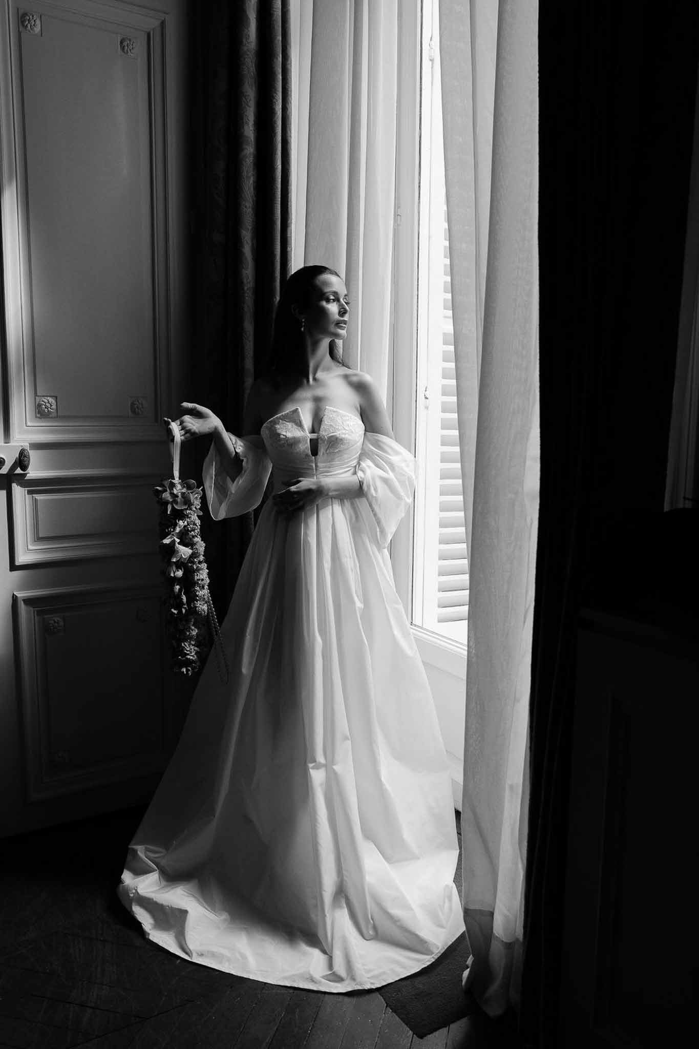 Black and white bride in ballgown with sheer organza sleeves beside tall window in boiserie-panelled room