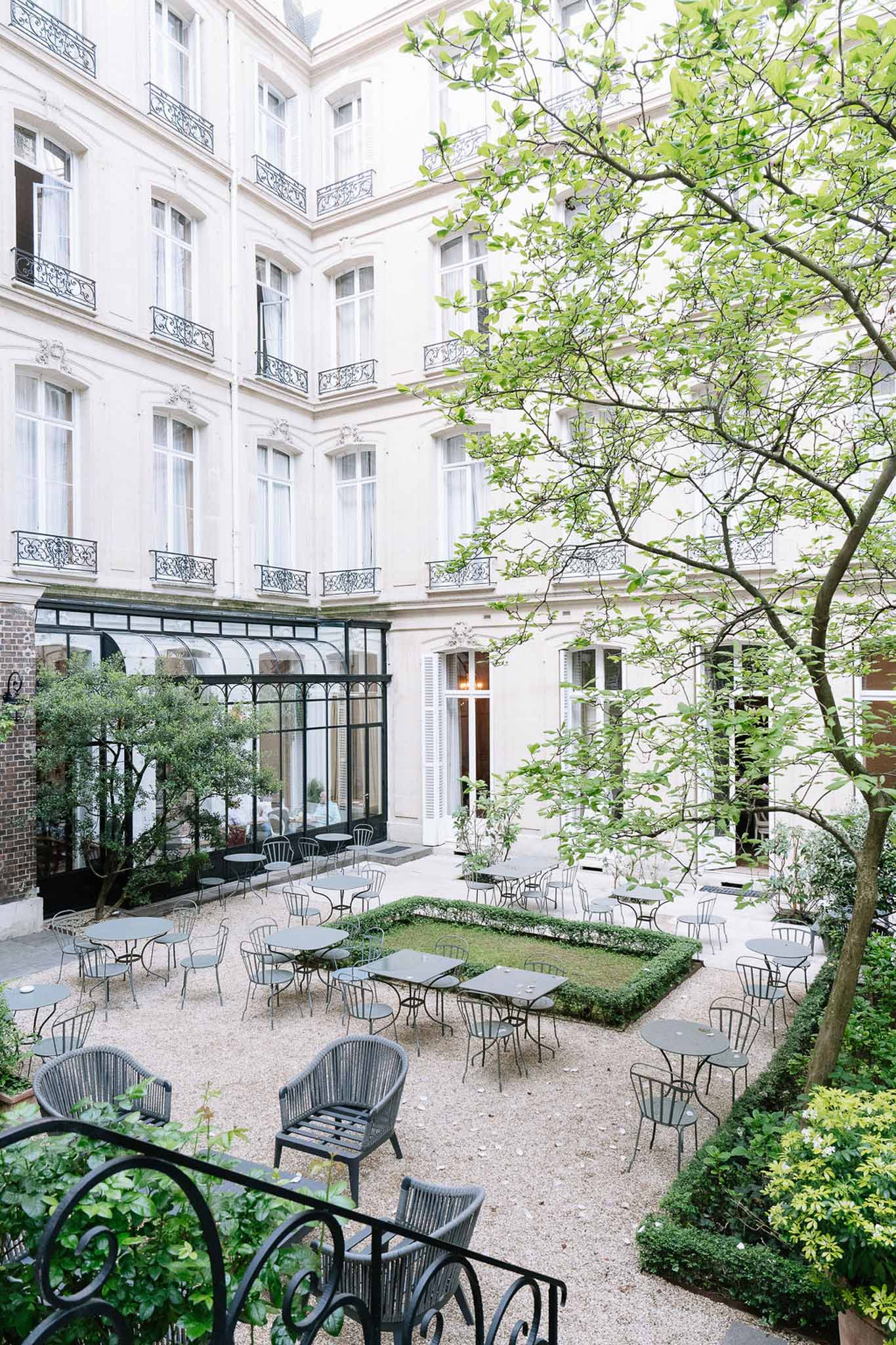 Aerial view of Parisian Haussmann courtyard with bistro tables, gravel surface, and glass greenhouse veranda