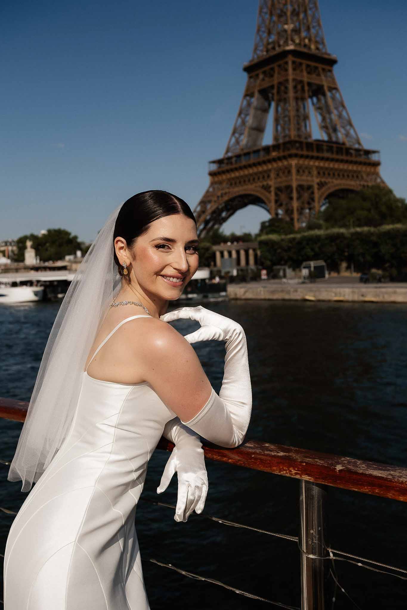 Bride in ivory satin gown with long gloves and cathedral veil on Seine River boat with Eiffel Tower behind