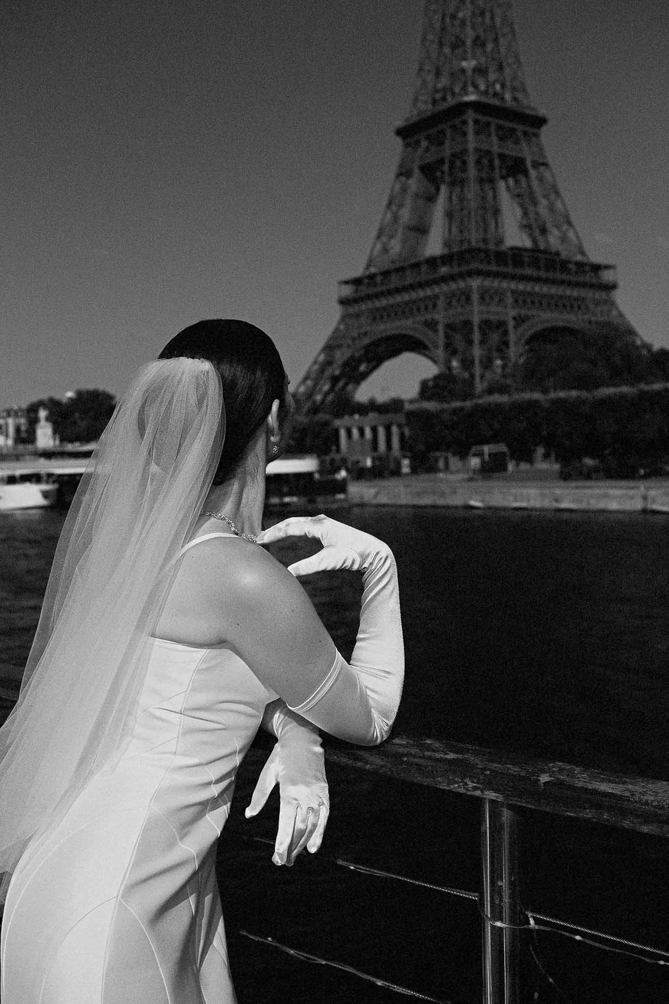 Black and white portrait of bride with satin gloves and cathedral veil overlooking Eiffel Tower