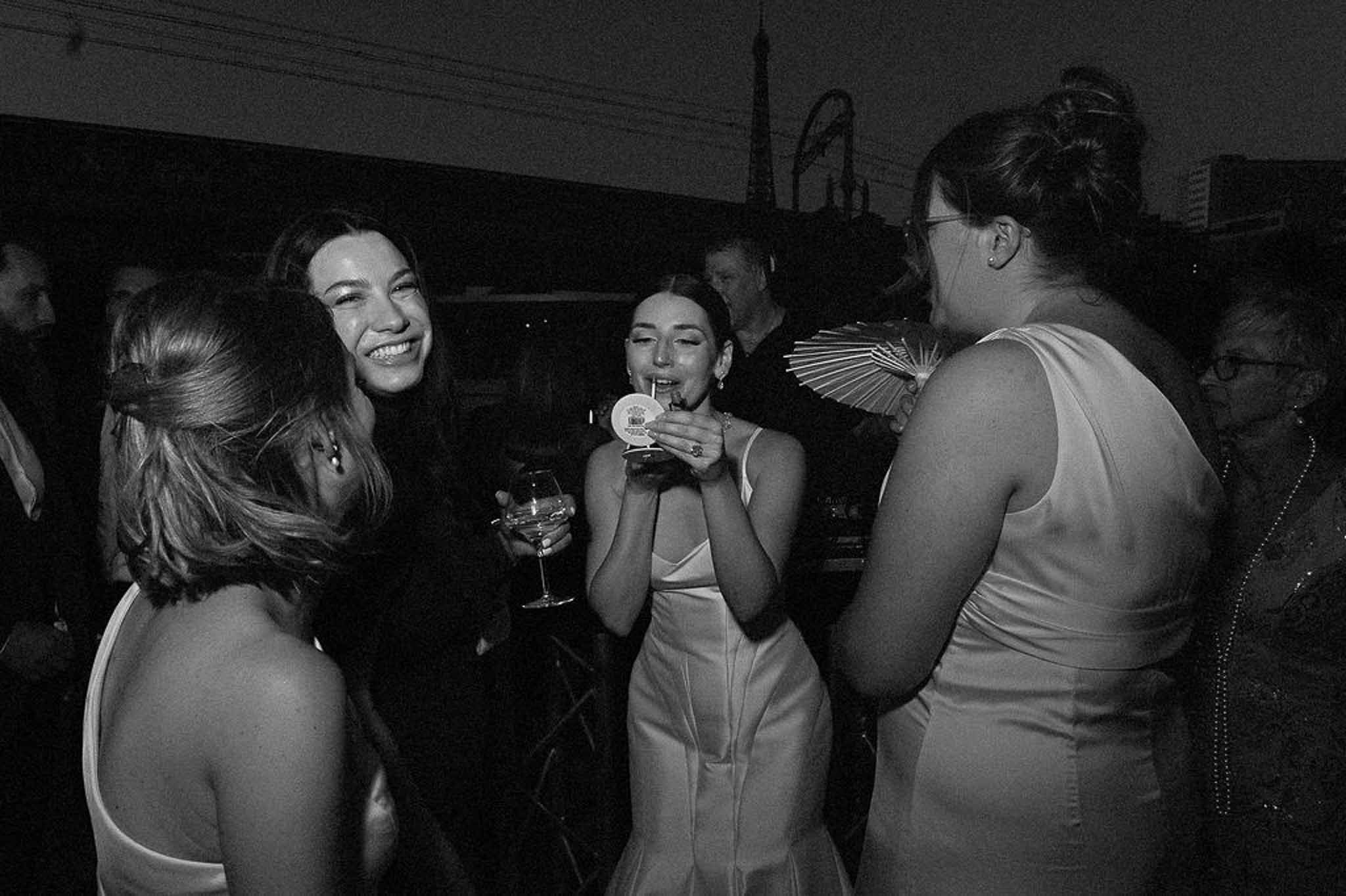 Black and white candid of bride and friends laughing with cocktails at dimly lit indoor reception