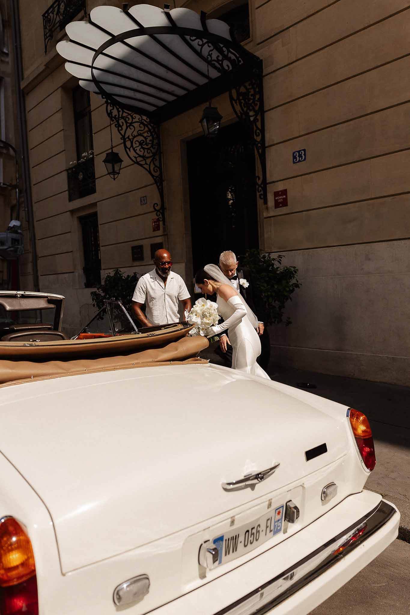 Bride in satin gown with long gloves and veil helped into vintage Rolls-Royce on Parisian street