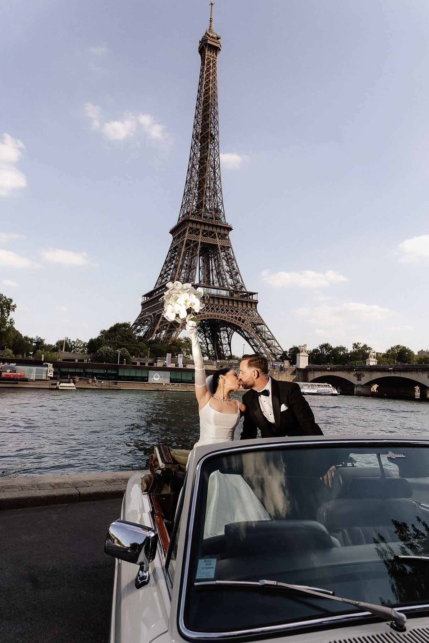 Couple kissing from vintage white convertible in front of Eiffel Tower with orchid bouquet