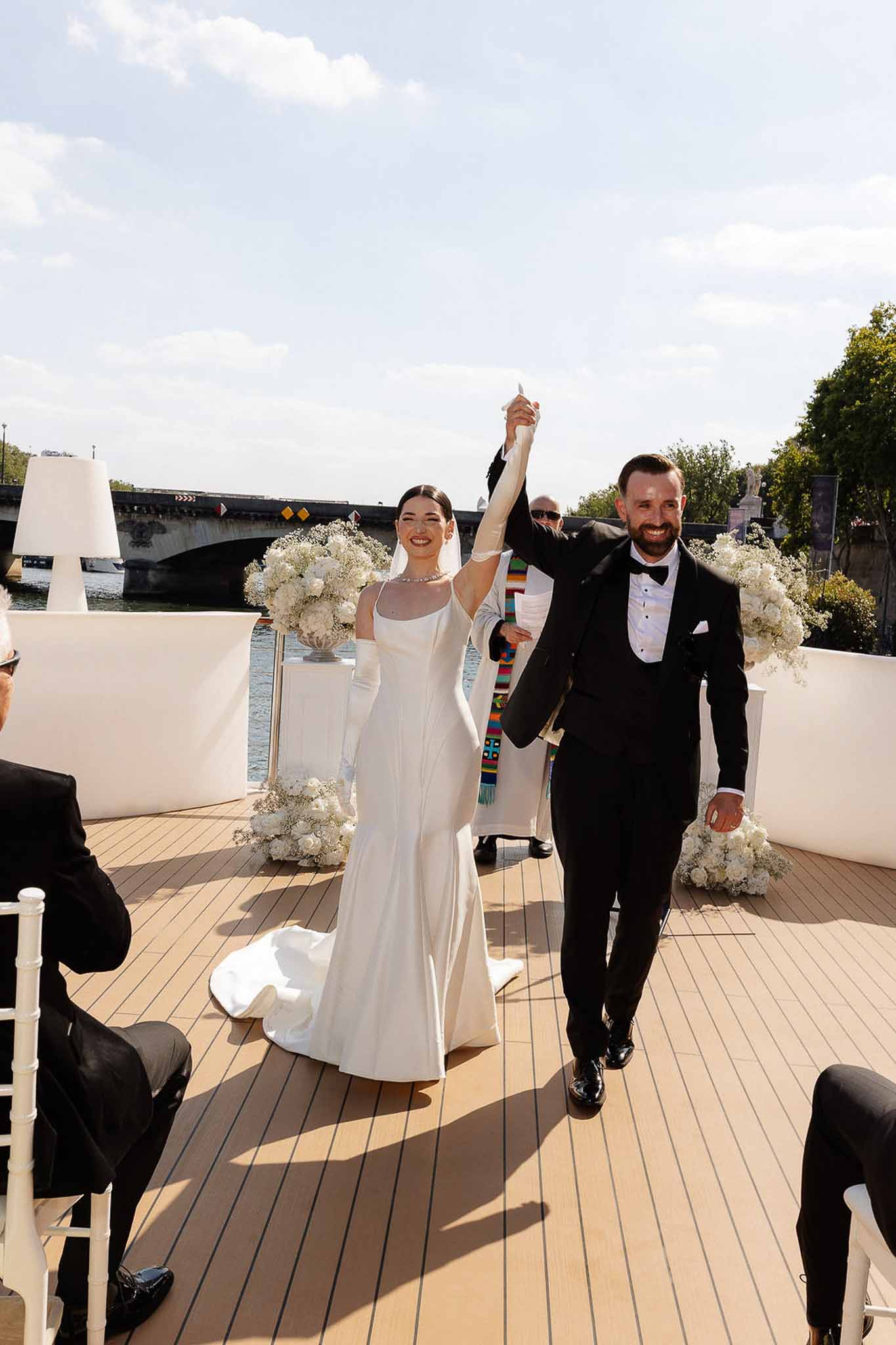 Couple raising joined hands after ceremony on Seine River boat with white rose arrangements