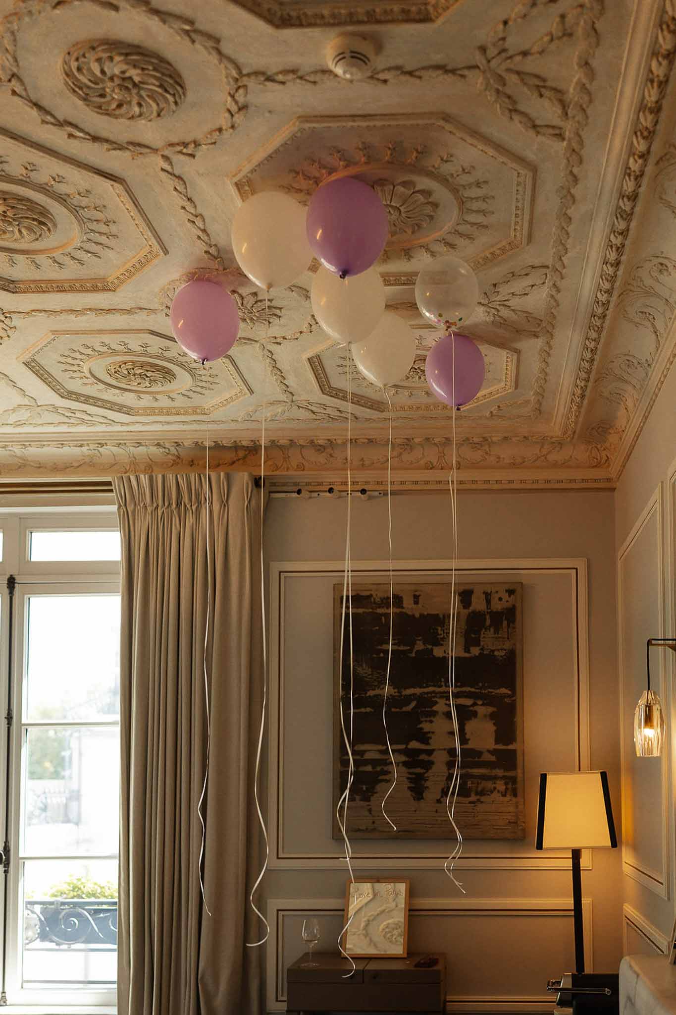 Lavender and white helium balloons floating against ornate gilt coffered ceiling in chateau bridal suite