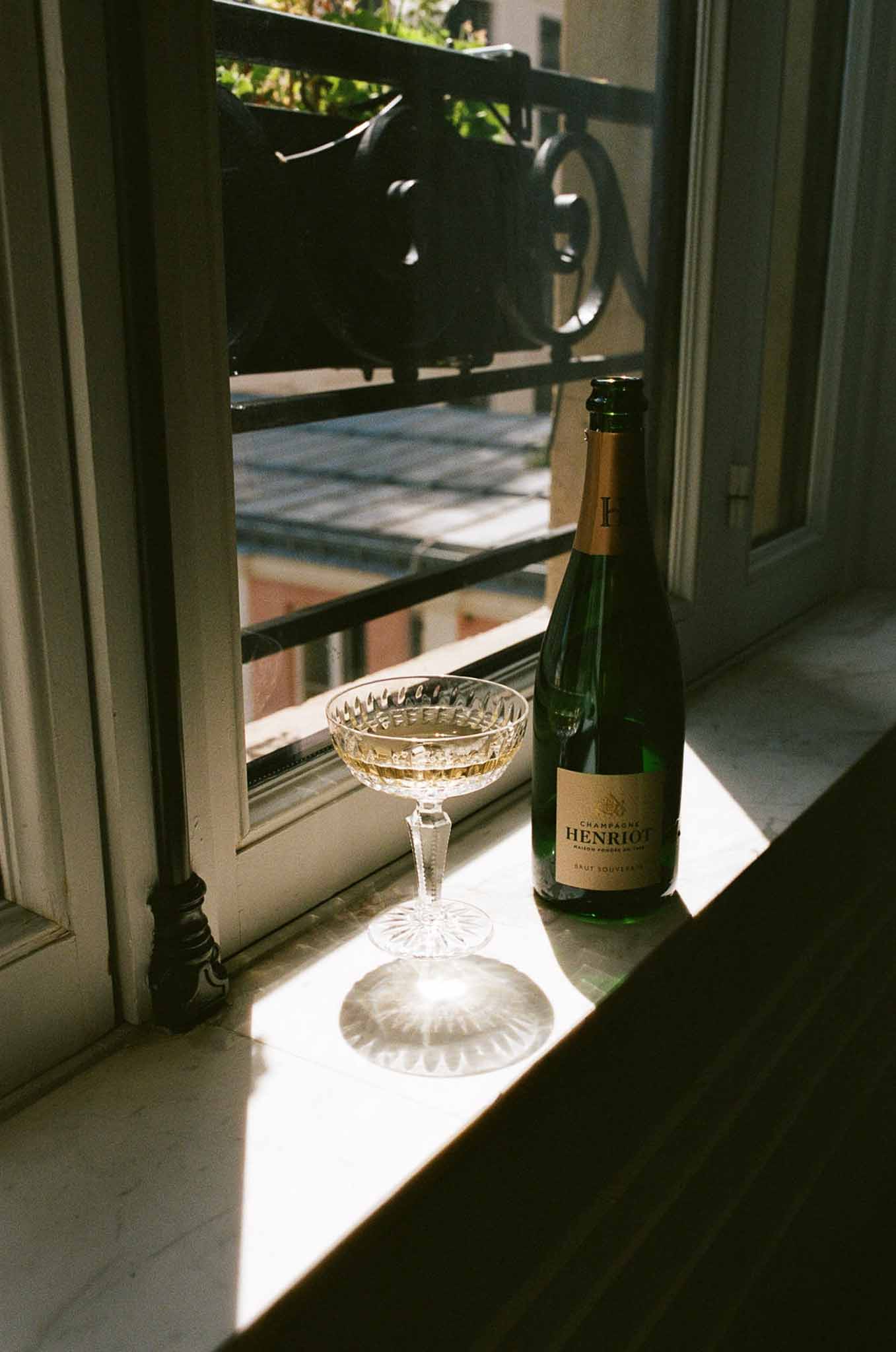 Henriot Brut Souverain champagne bottle and crystal coupe glass on stone window ledge with sunlight starburst shadow