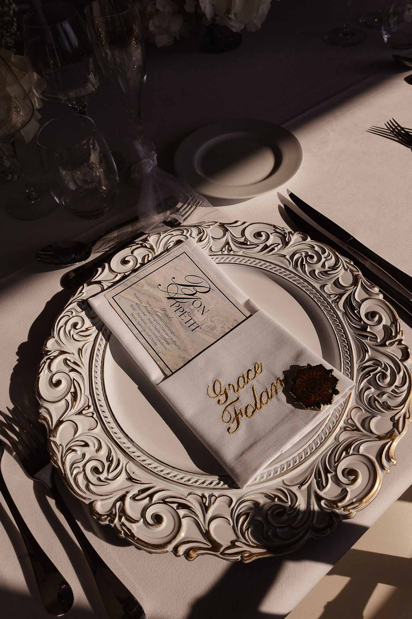 Reception place setting with gold baroque charger plate, white napkin, Bon Appetit menu card, and black cutlery
