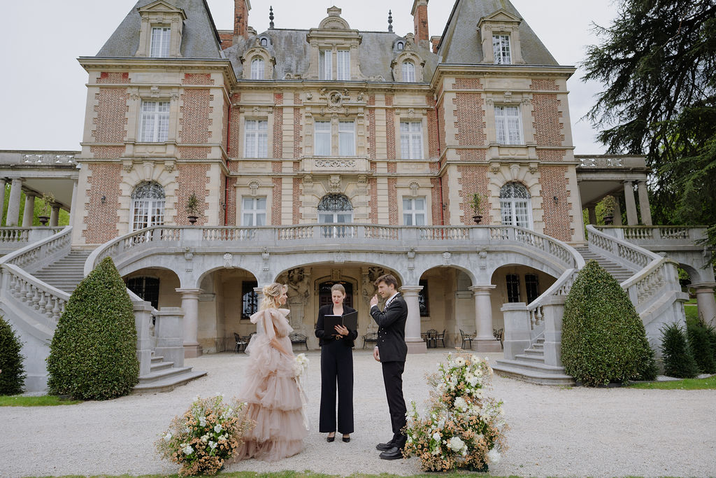 Bride in blush gown and groom at outdoor ceremony on gravel forecourt of grand French chateau