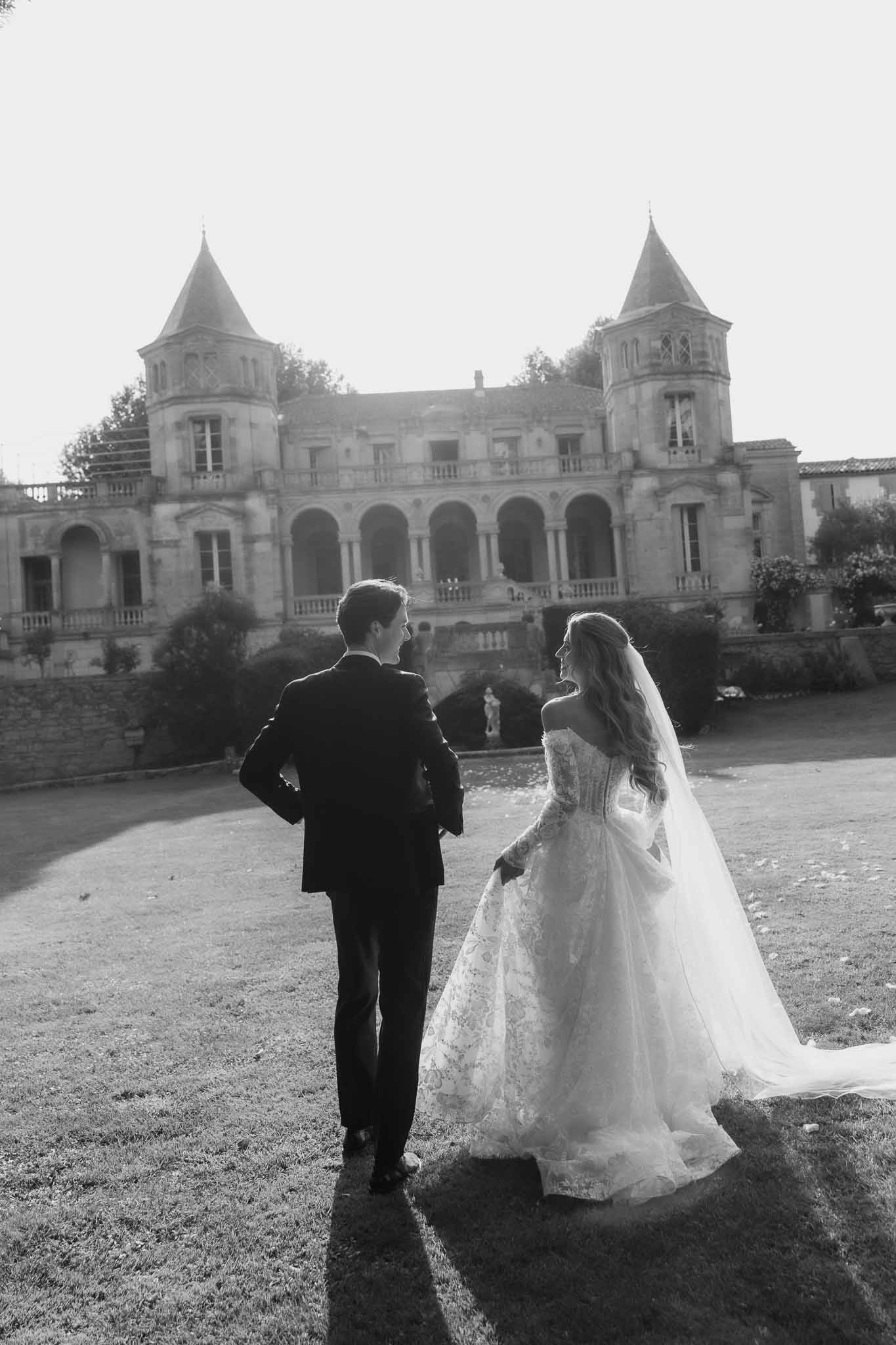 Black-and-white rear view of couple walking toward a turreted French chateau with colonnades and balustrades