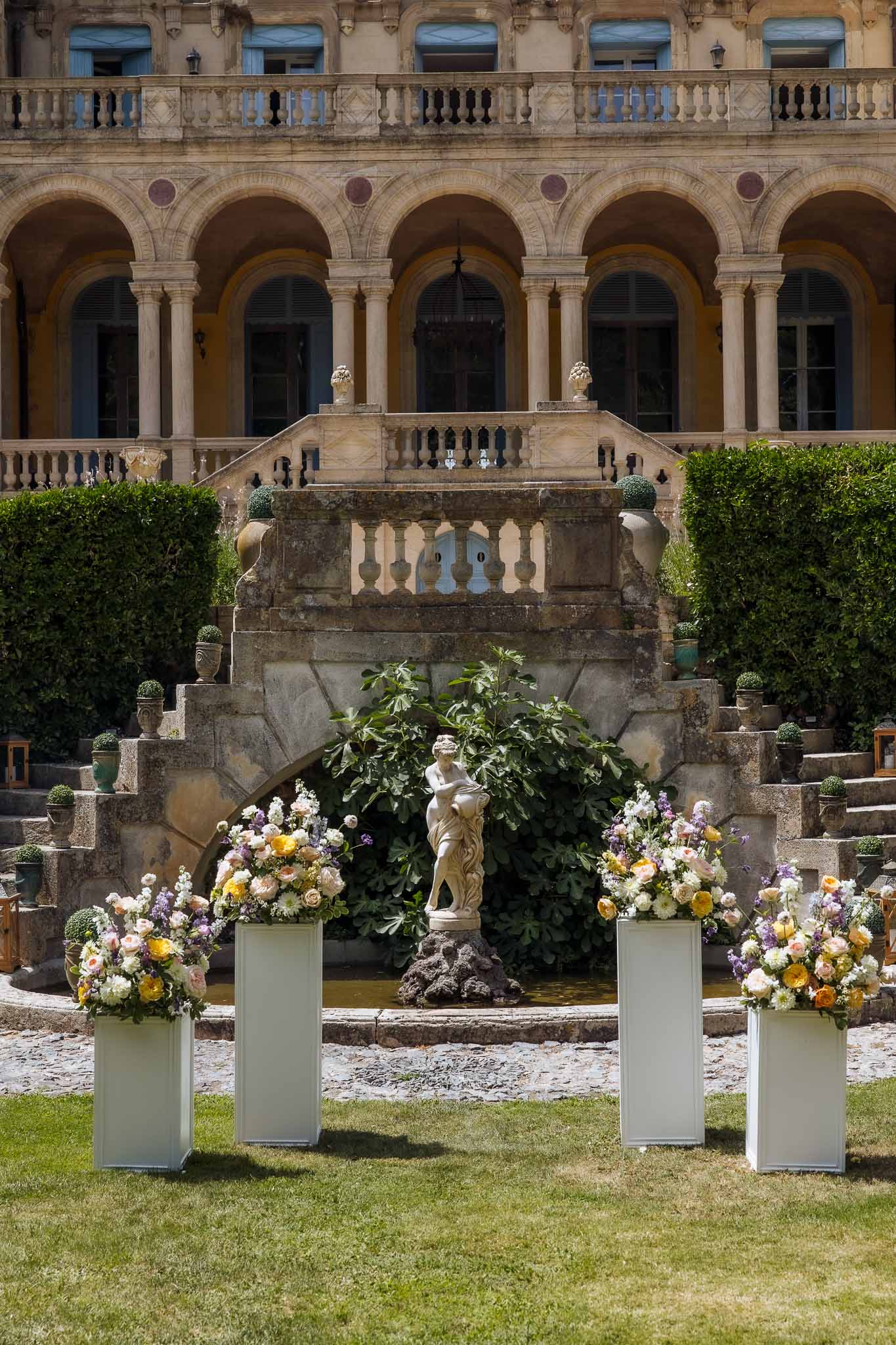 Outdoor ceremony setup in classical chateau garden with floral pedestals in peach and lavender tones