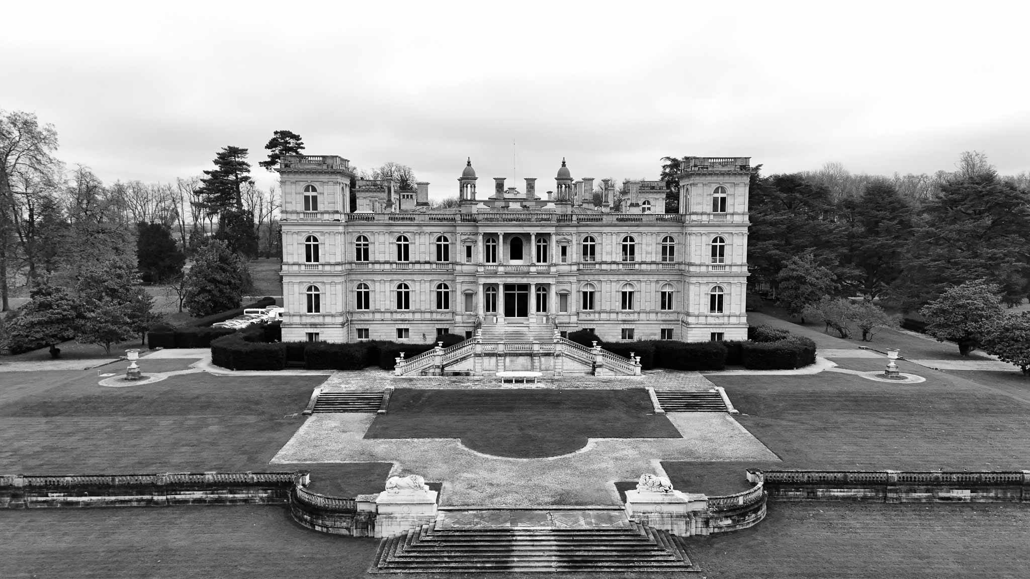 Black-and-white aerial drone shot of neoclassical chateau with formal parterre gardens and stone terraces