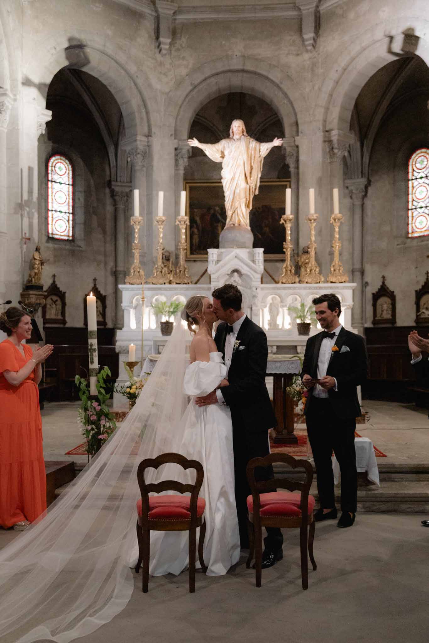 Bride and groom share first kiss at altar of French stone church with stained glass windows