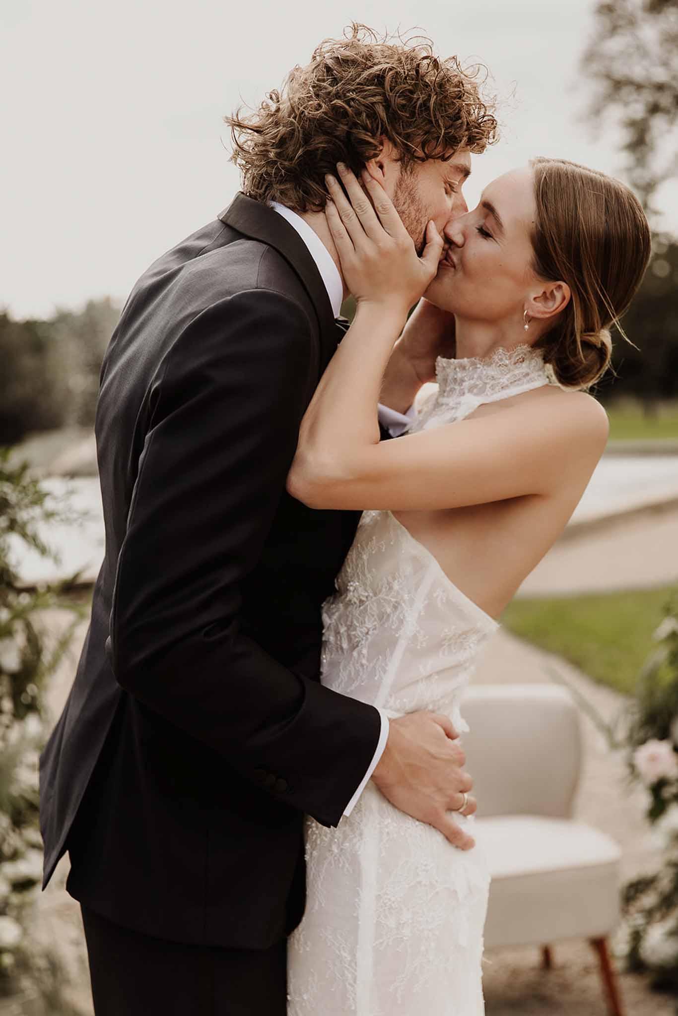 Close-up of bride and groom first kiss during outdoor ceremony with pool and pink florals behind