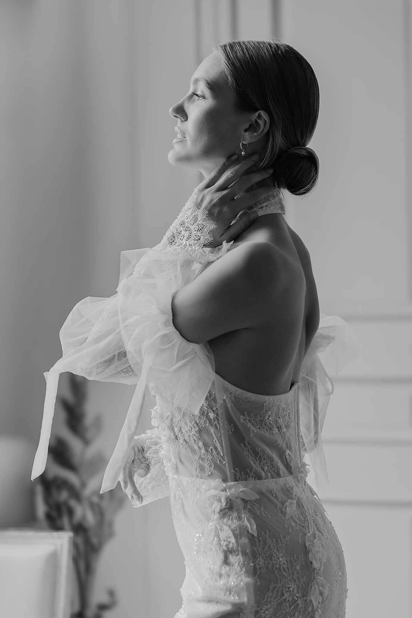Black and white profile portrait of bride in open-back lace gown with tulle wrap, hair in low bun
