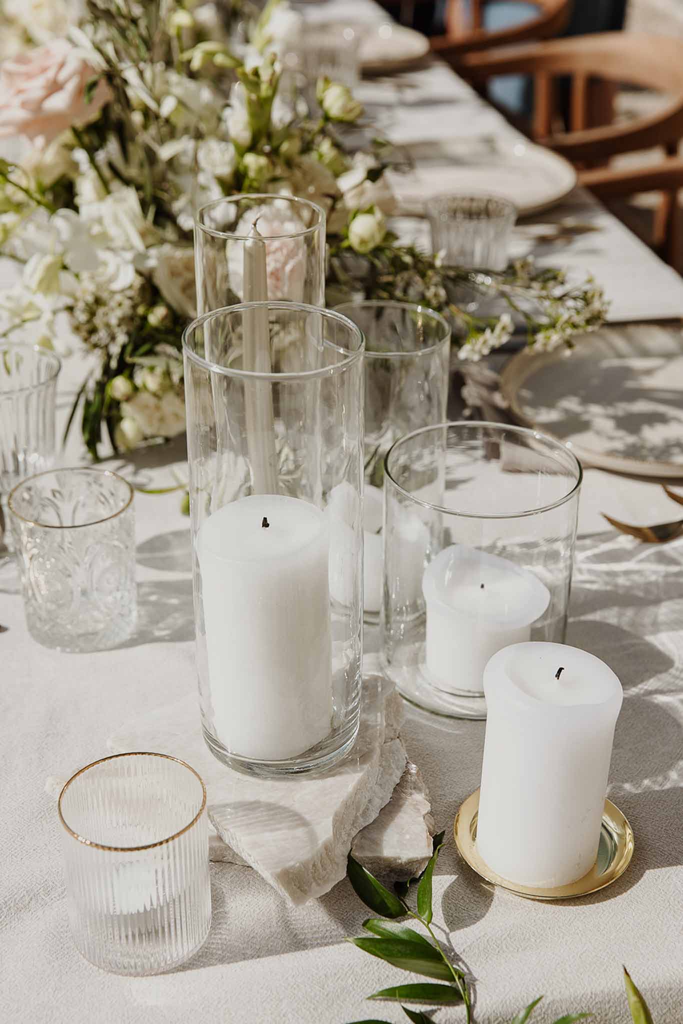 Reception table with white pillar candles in glass cylinders, blush and white floral centerpiece, and gold-rimmed glassware