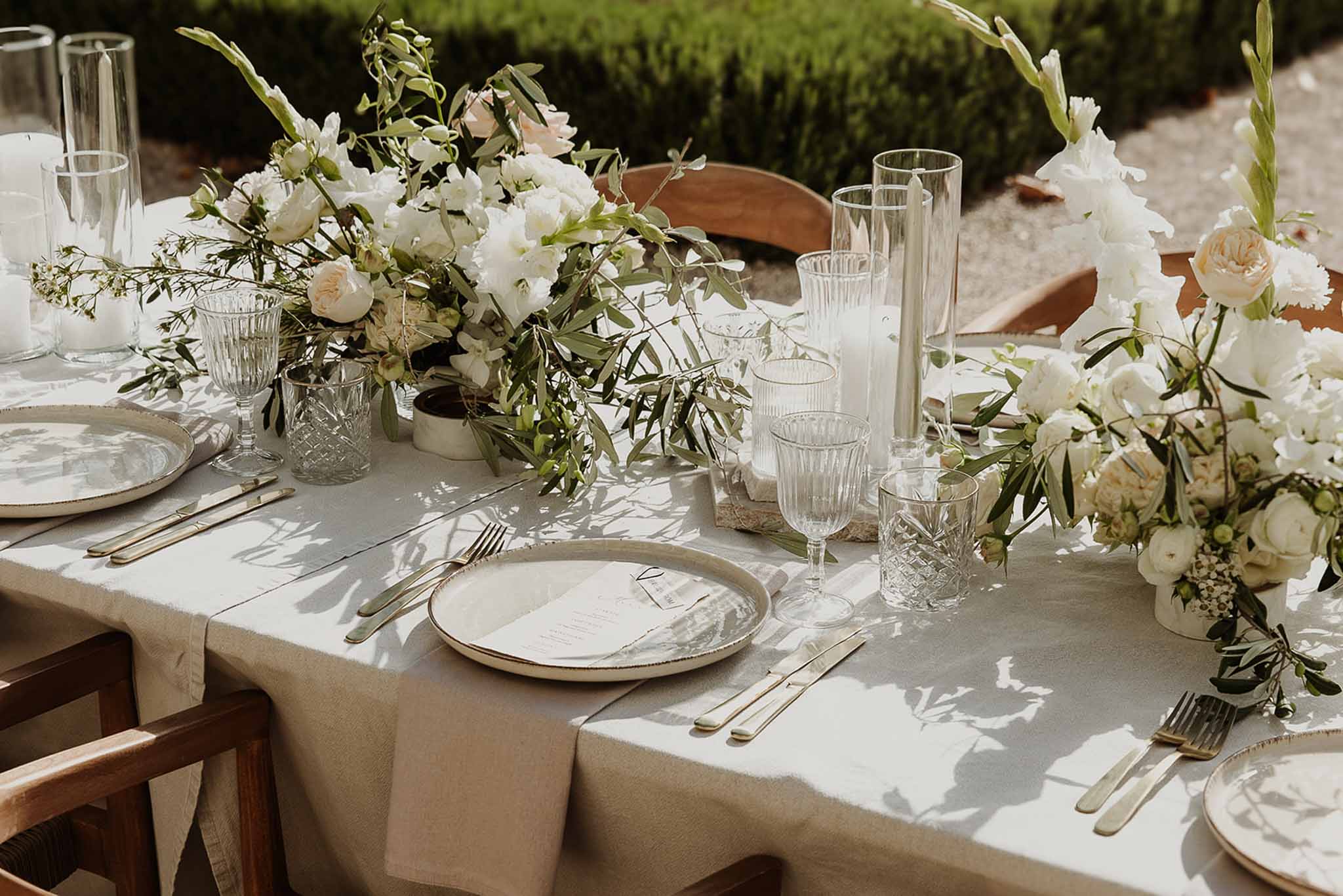 Place setting with matte ceramic plate, gold flatware, and low garden roses with olive branch centerpiece