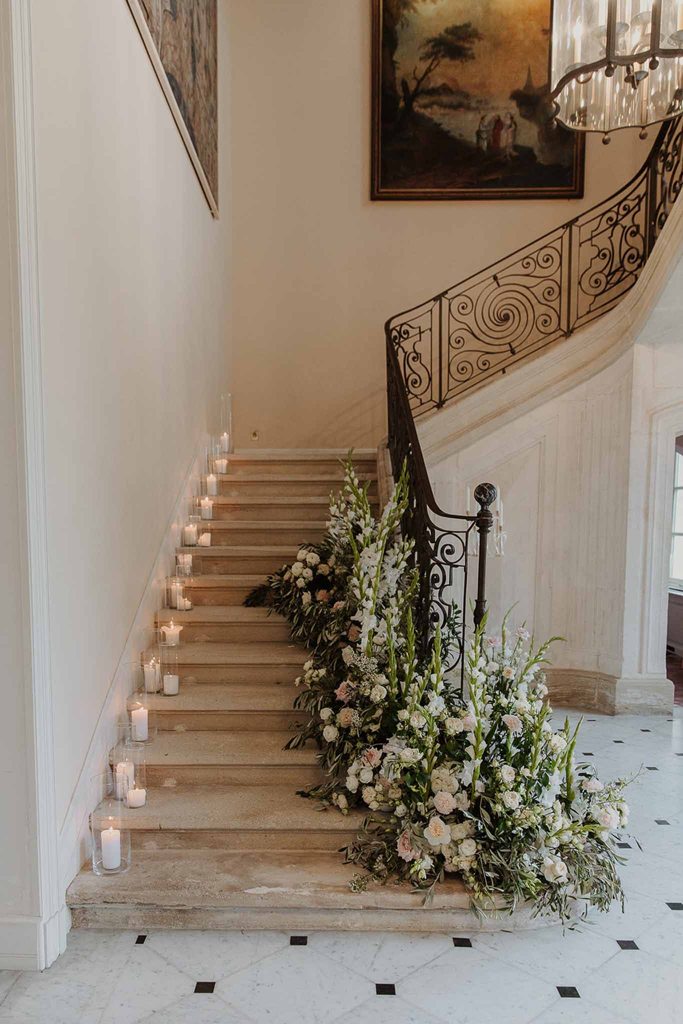 Chateau staircase decorated with cascading white and blush roses, eucalyptus, and lit pillar candles for a wedding