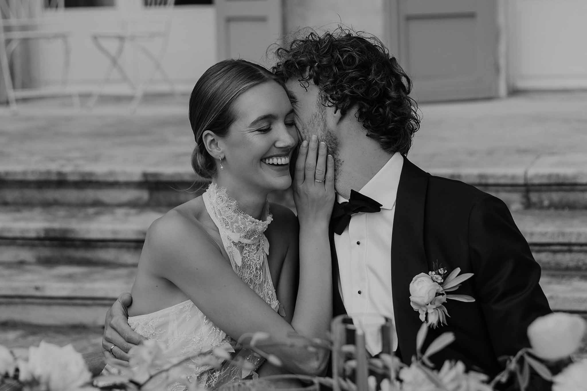 Black and white close-up of groom kissing bride cheek as she smiles with eyes closed