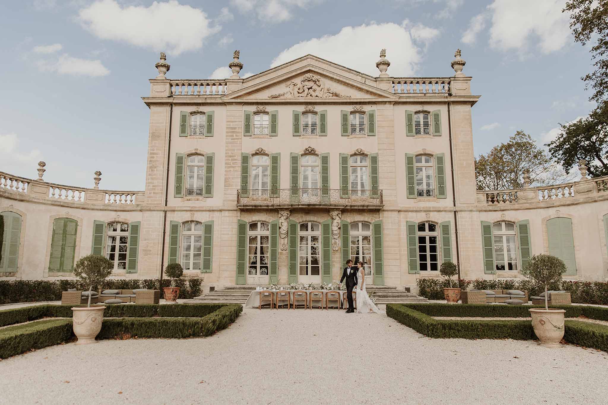 Bride and groom standing before a reception table on the gravel forecourt of a three-story French chateau