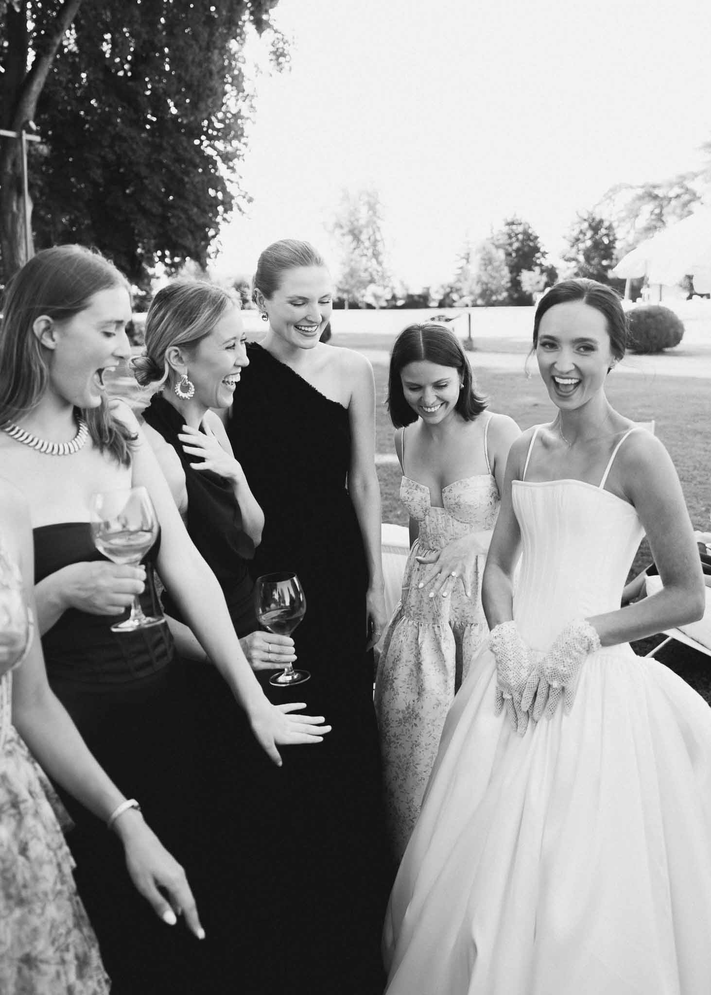 Black and white photo of bride laughing with four female guests holding wine glasses during cocktail hour