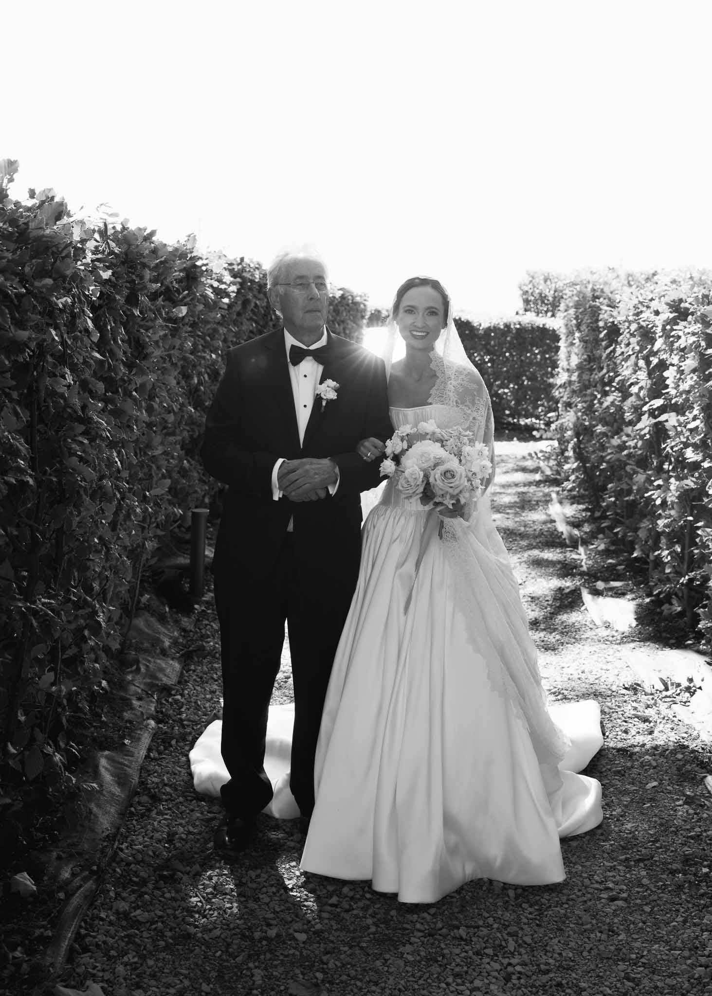 Black and white photo of bride and groom walking hand in hand in a garden
