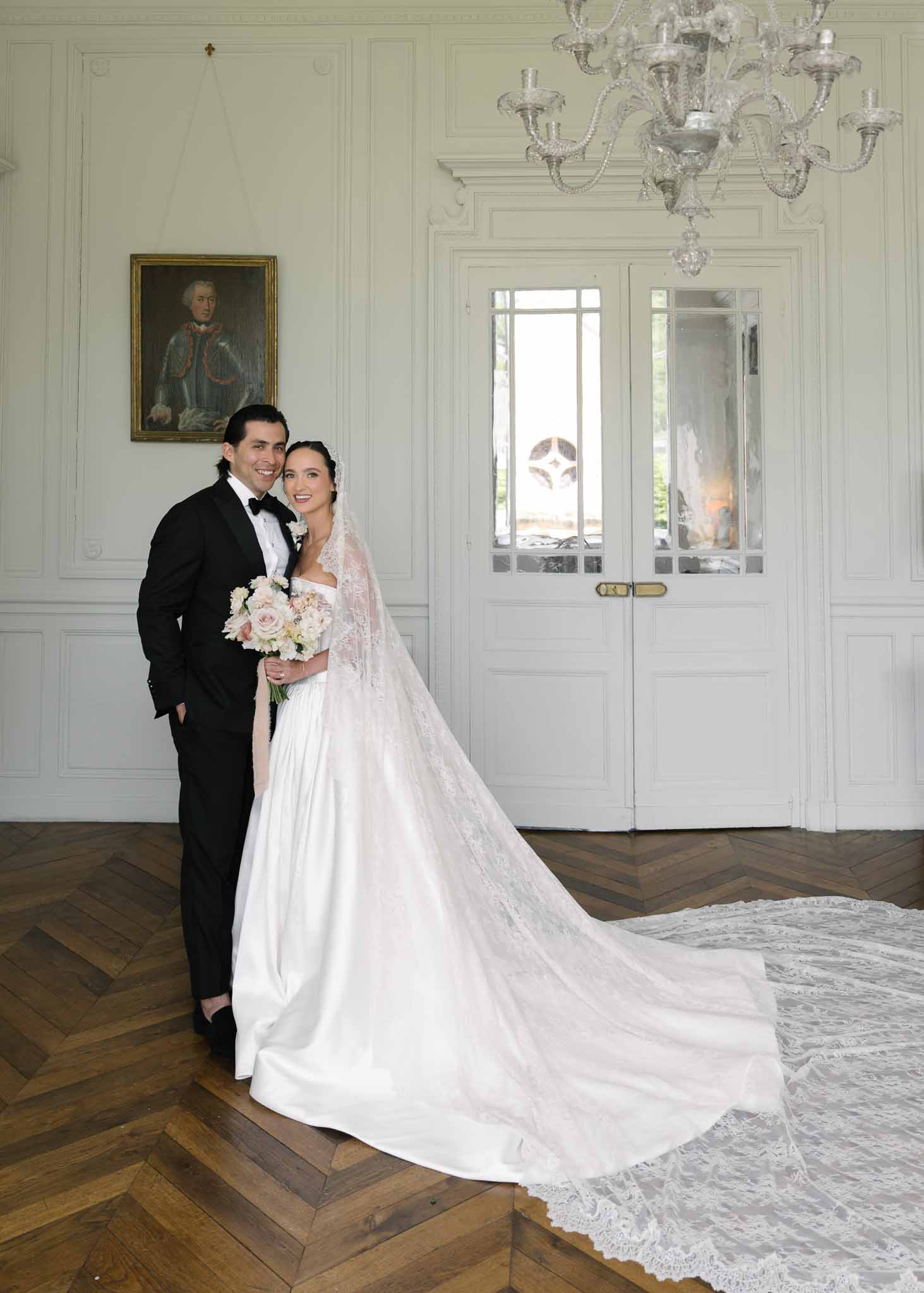 Couple portrait in chateau salon with bride in ivory ball gown and cathedral veil on parquet floor